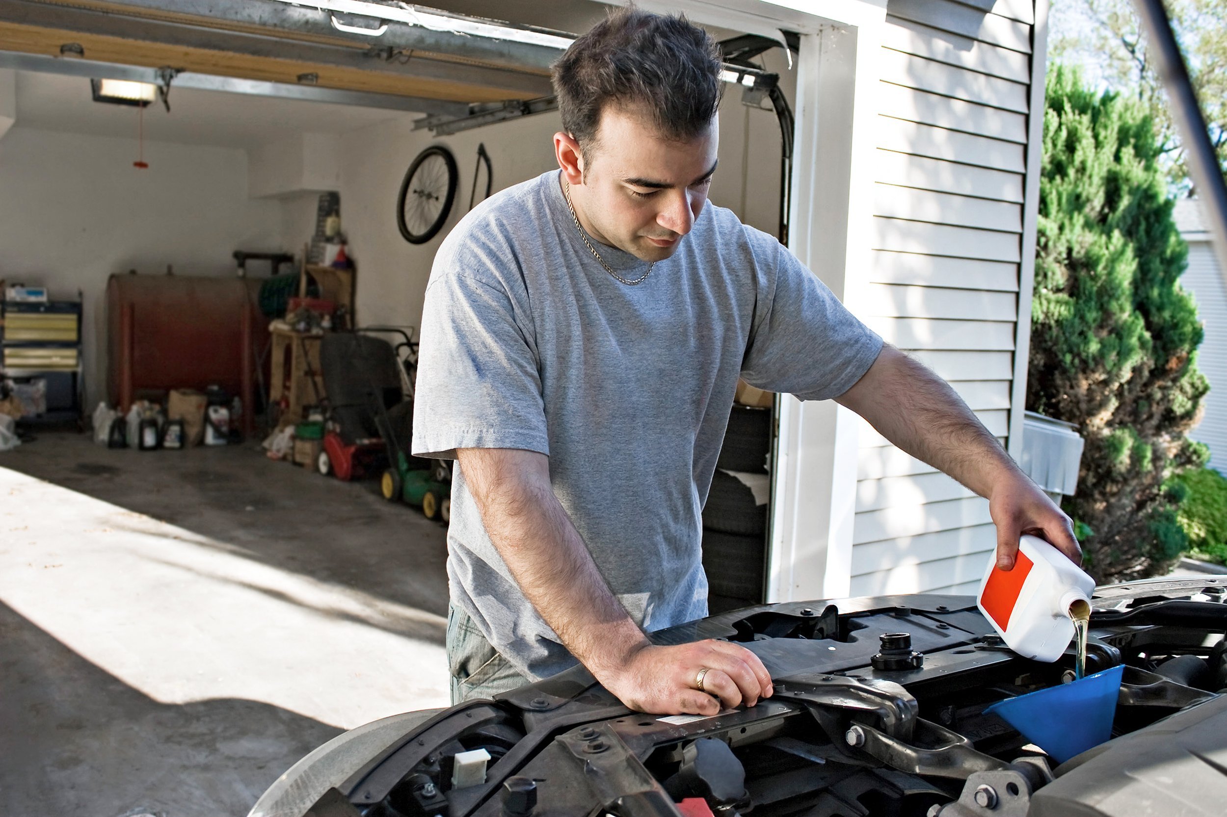young man adding oil to his cars engine