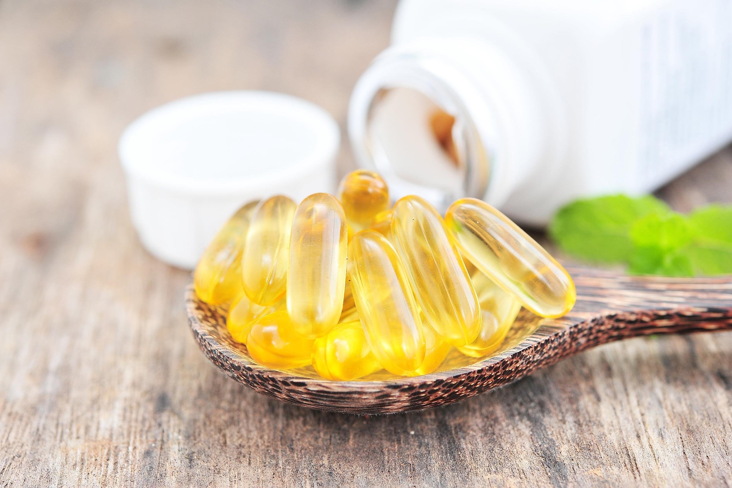 cod liver oil omega 3 gel capsules on wooden spoon