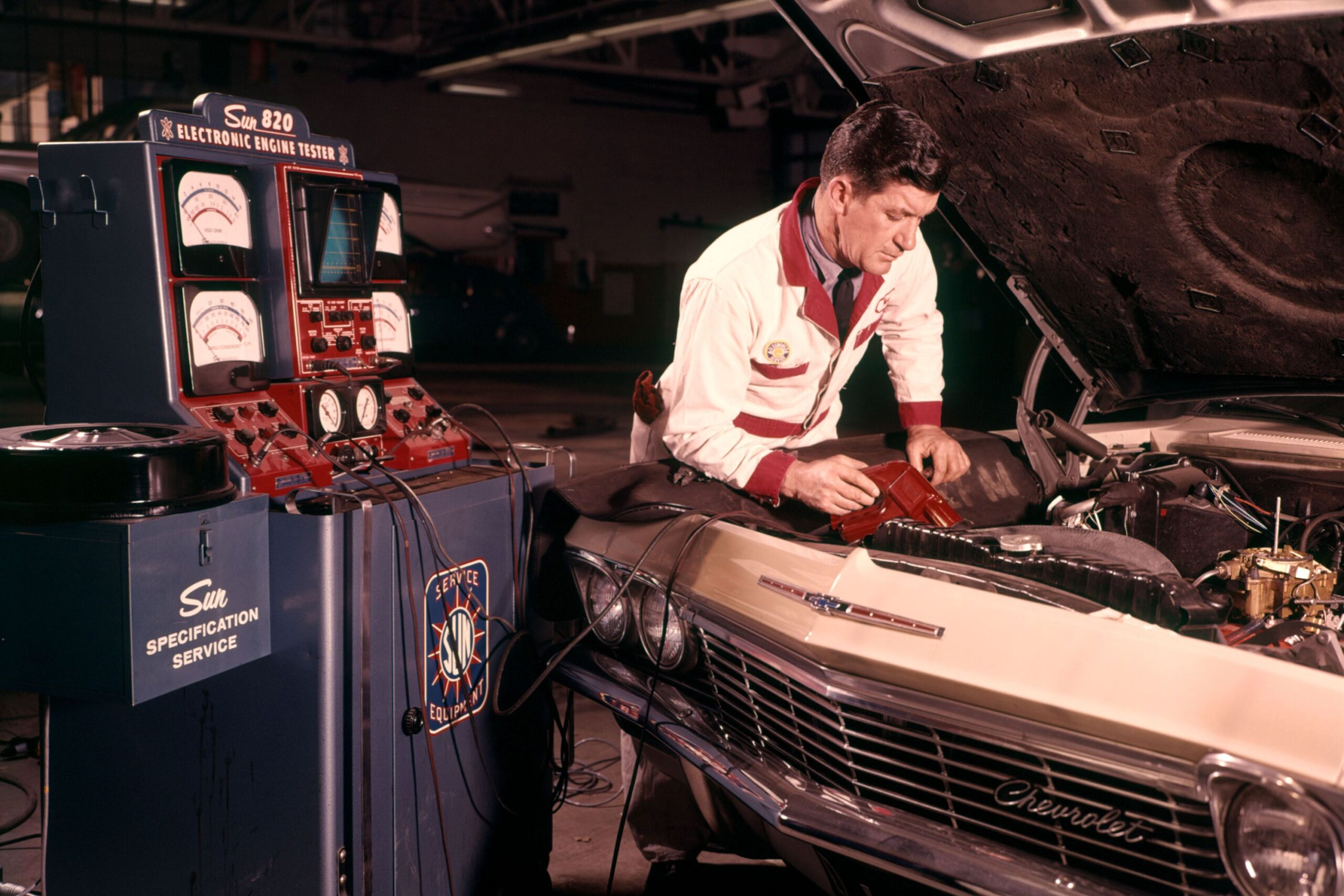 1960s MAN AUTO MECHANIC WORKING ON CAR ENGINE CONNECTED TO DIAGNOSTIC EQUIPMENT
