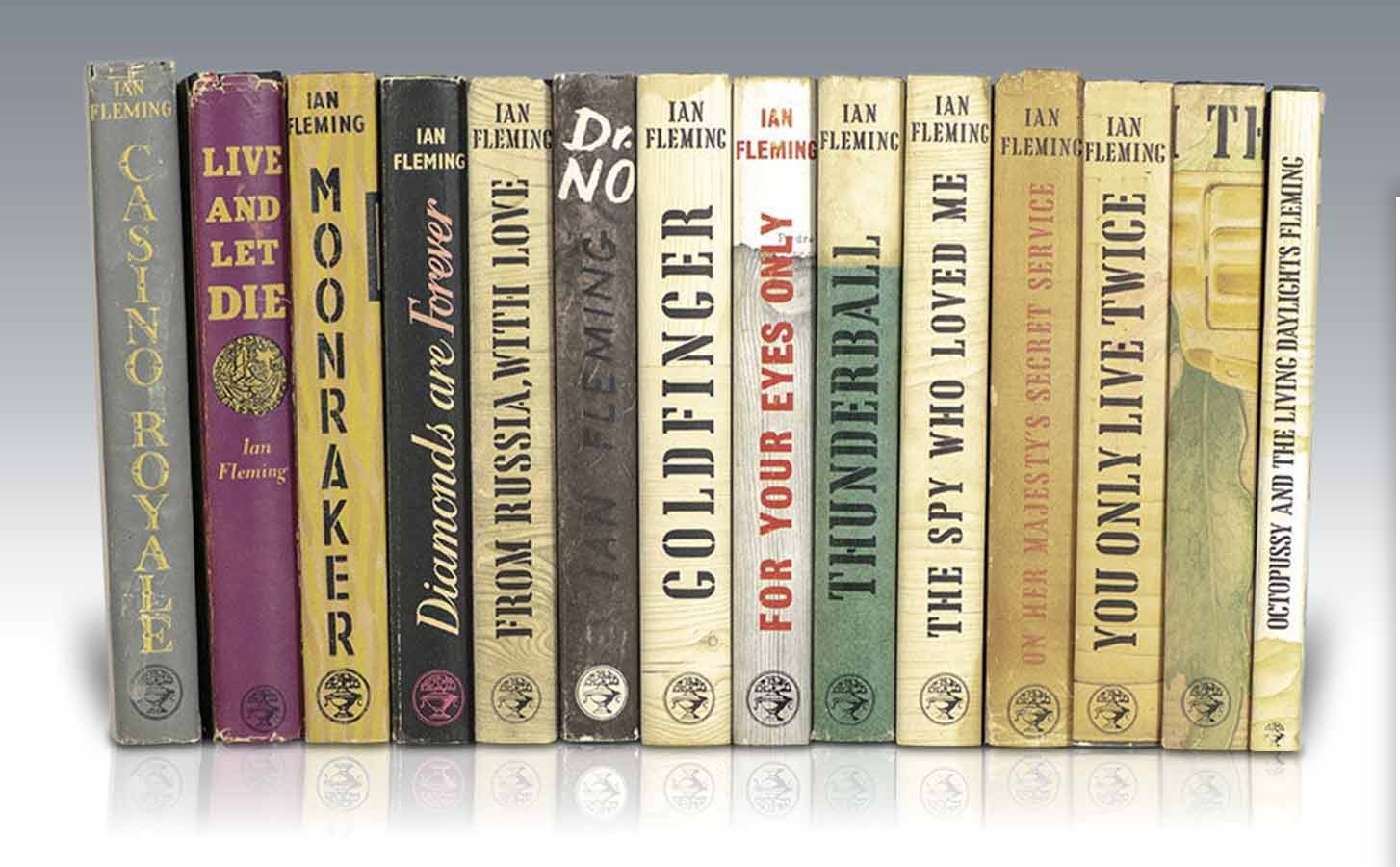 Spines of fourteen paperback books by Ian Fleming lined together on Biblio.com on a white table, 06/14/21, with a greyscale background