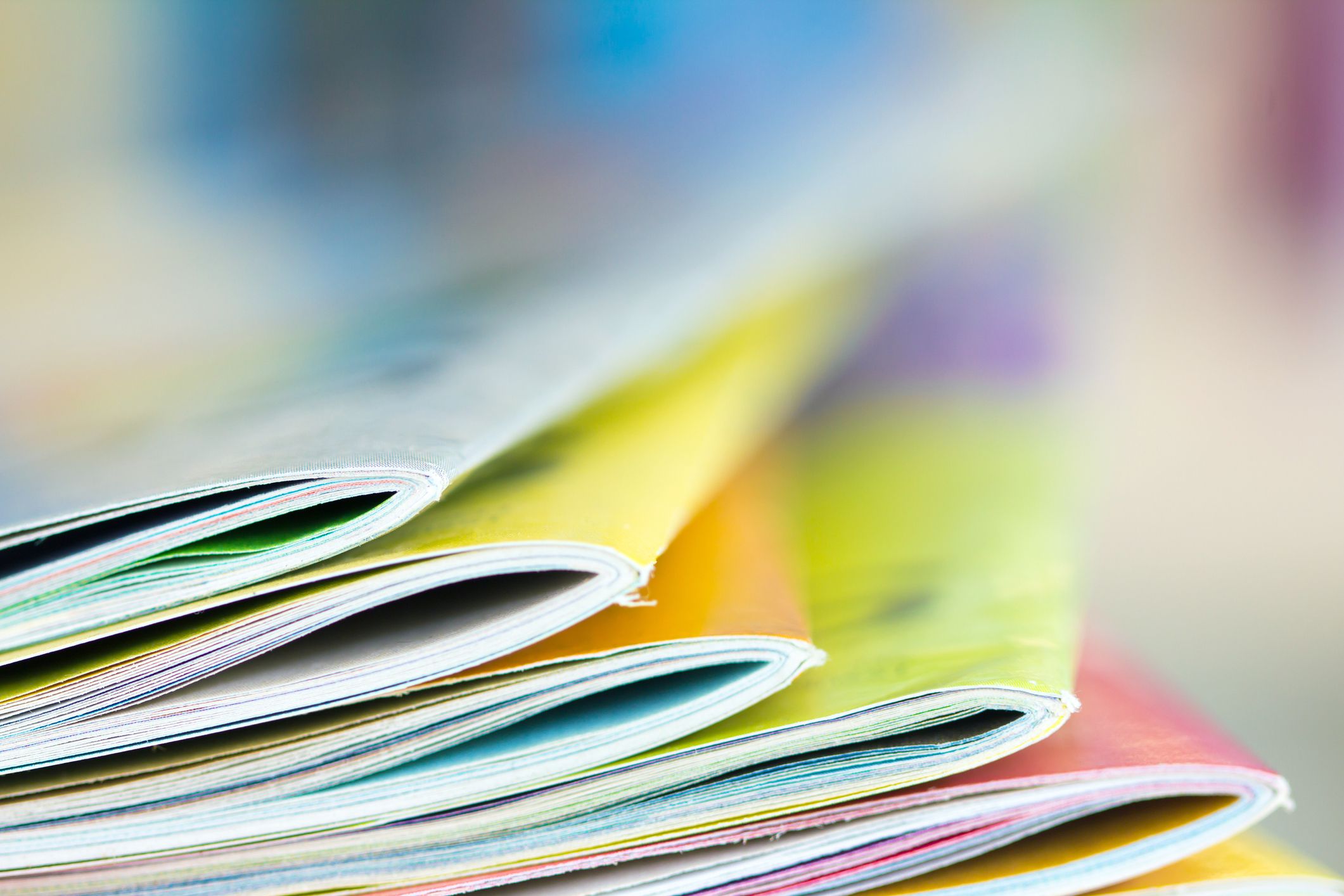 Close up edge of colorful magazine stacking with blurry bookshelf background for publication and publishing concept , extremely DOF