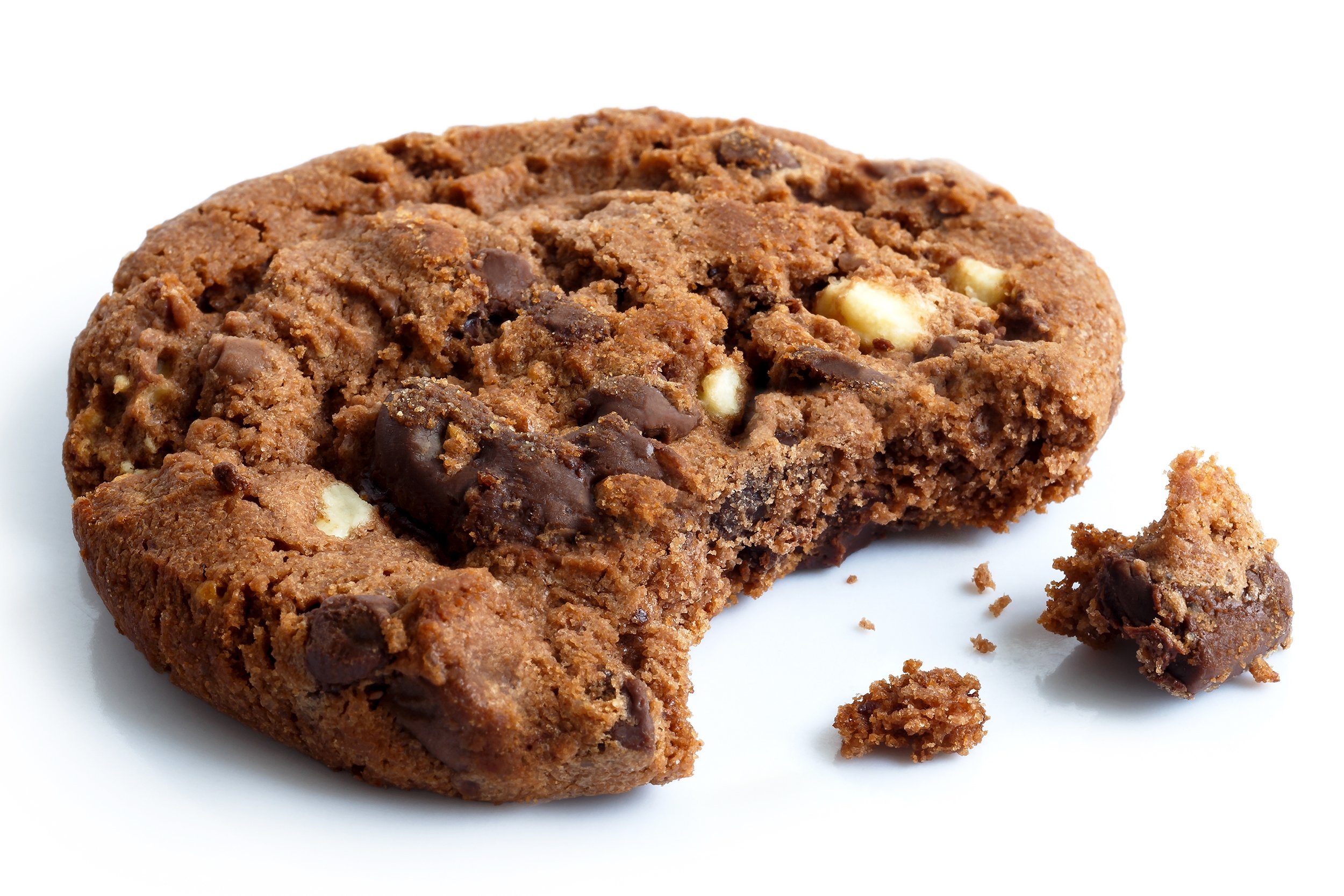A chocolate chip cookie with a bite taken out of it sits on a white surface, with a few crumbs and a small broken piece nearby.