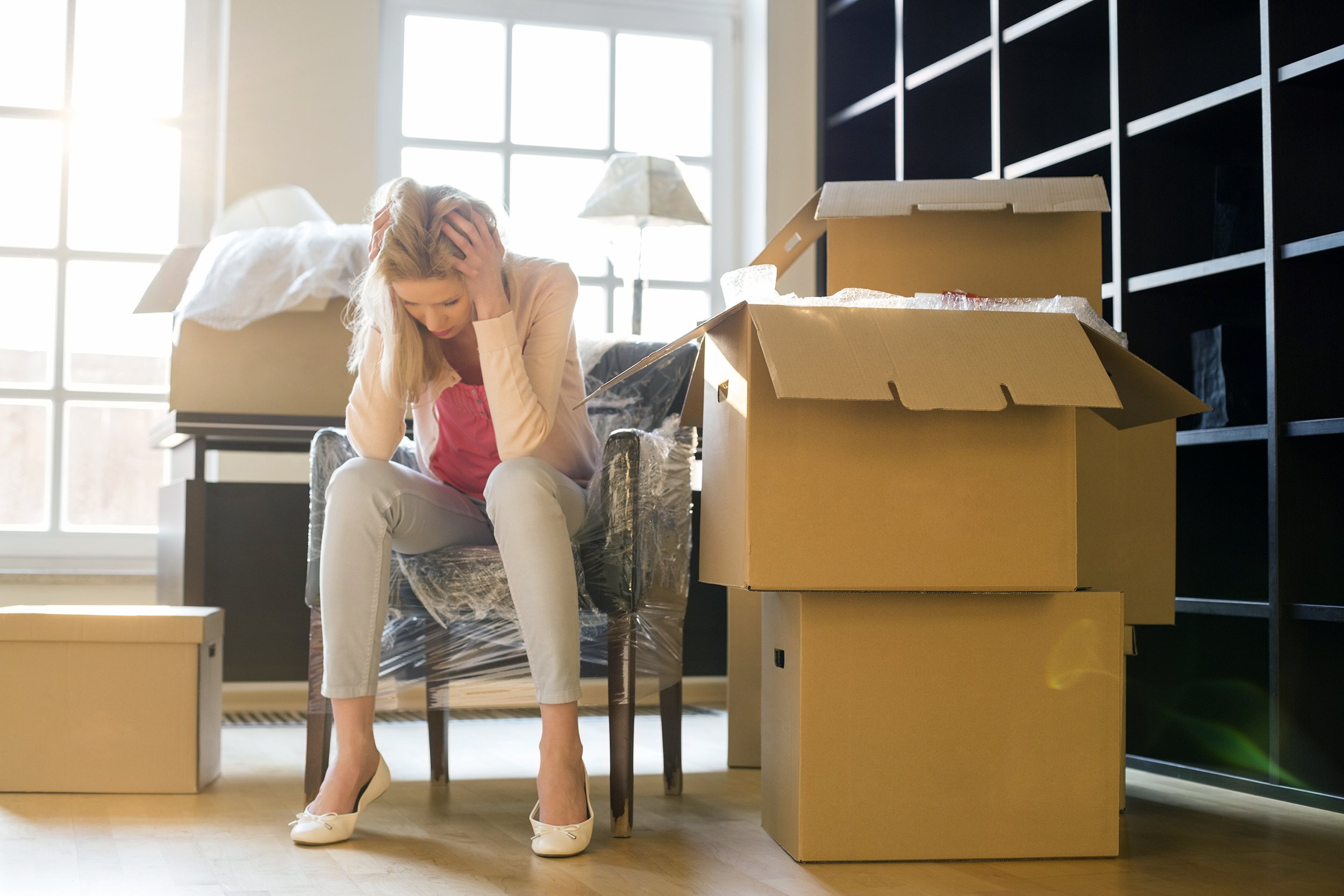 frustrated woman sitting by cardboard boxes in new house