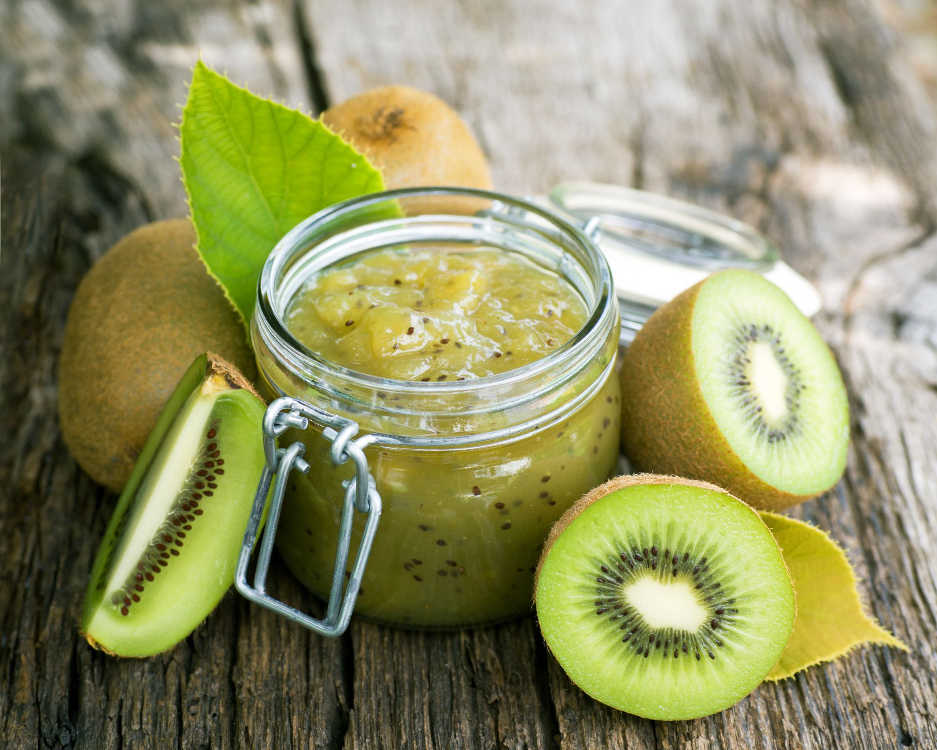 close-up of jar of kiwi jam and sliced kiwi on wooden table