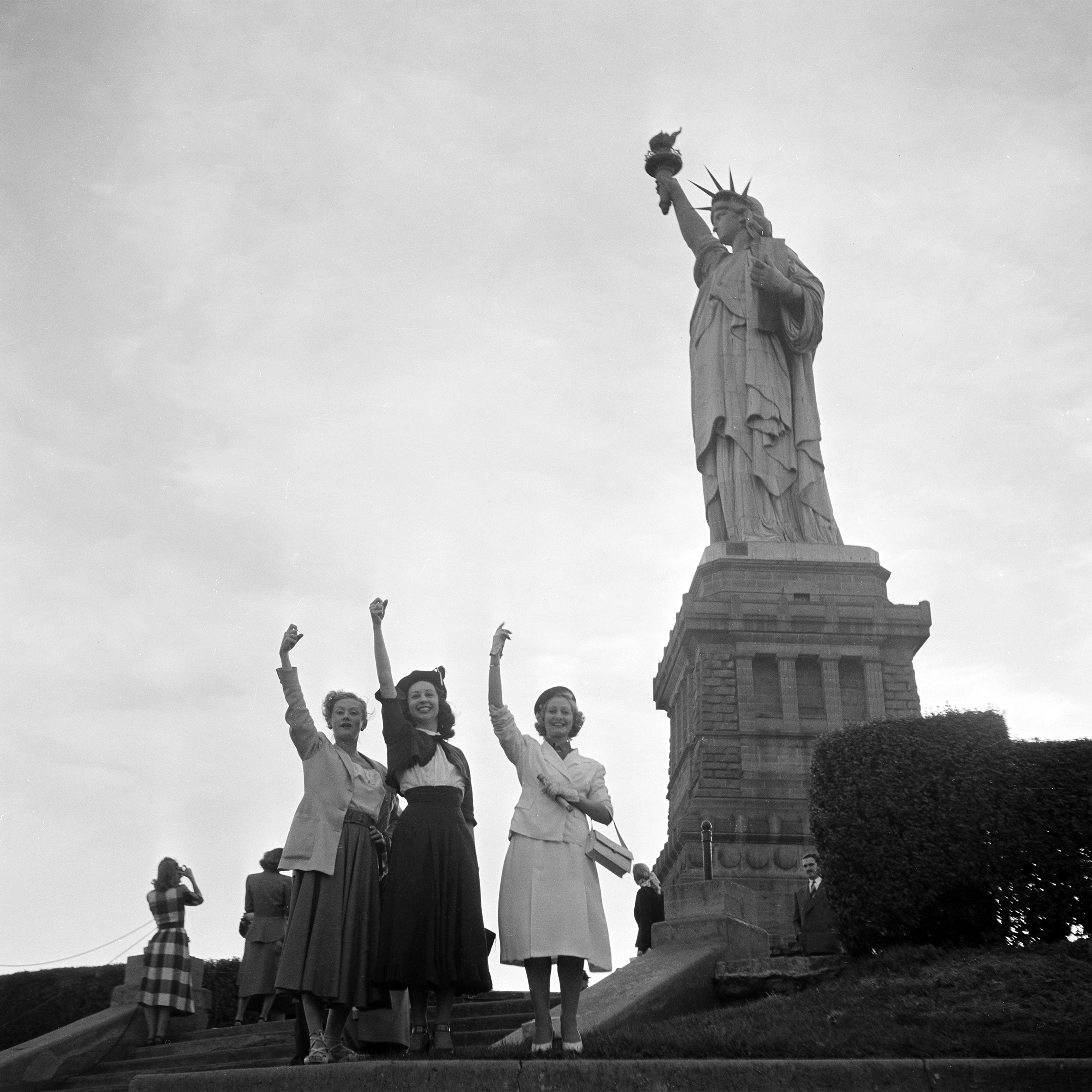 Three women pose underneath the Statue of Liberty on Ellis Island in New York