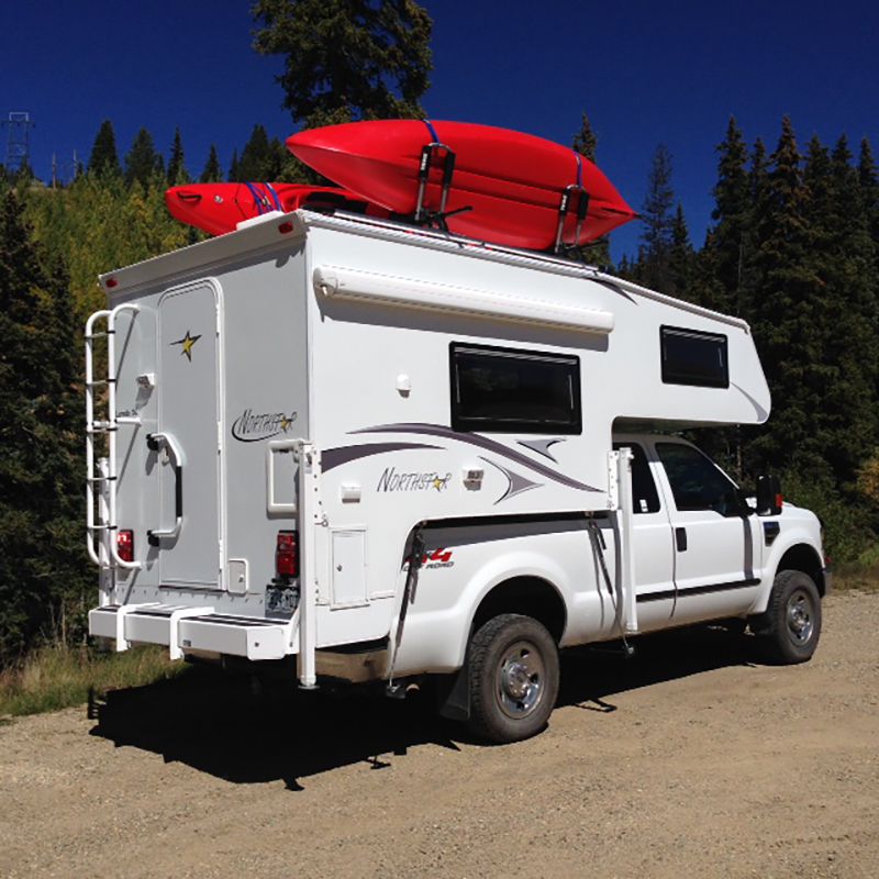 Northstar Laredo Truck Camper in forest with two red kayaks on roof
