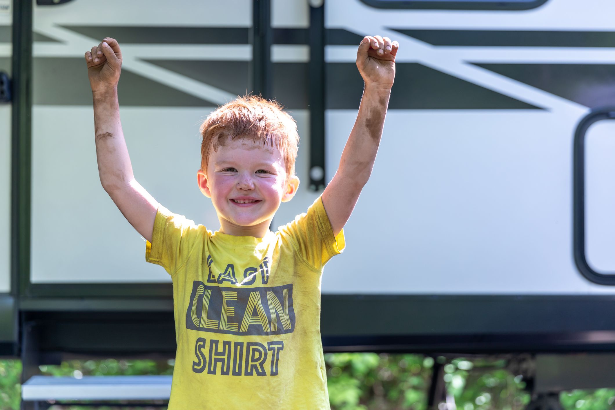 Mud Covered little boy smiling while standing outside the Camper Trailer in Summer