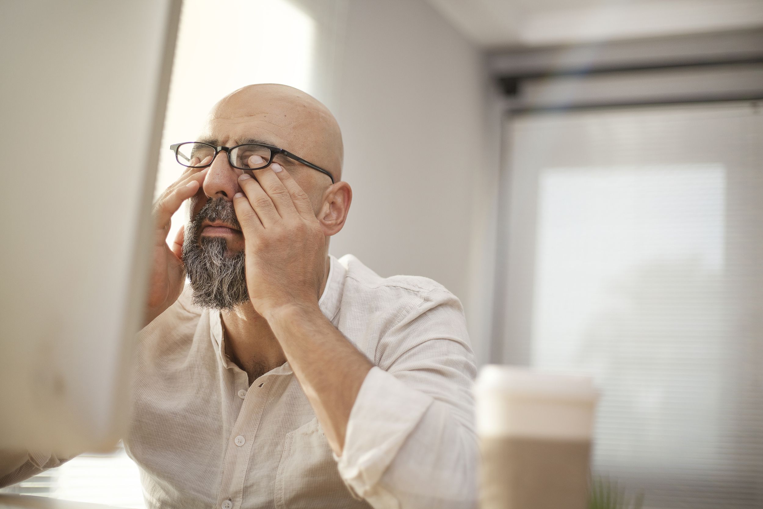 senior businessman rubbing his tired eyes in front of computer