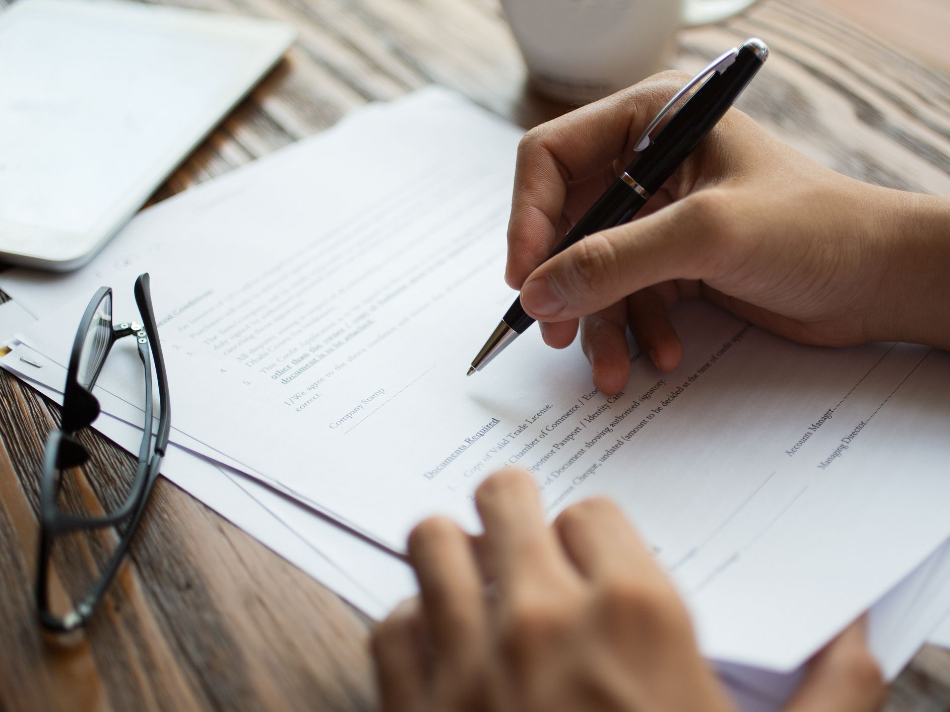 Unrecognizable businessman examining papers at table. Manager with ballpoint pen filling business papers. Close-up of male hands working at desk. Analyzing documents concept