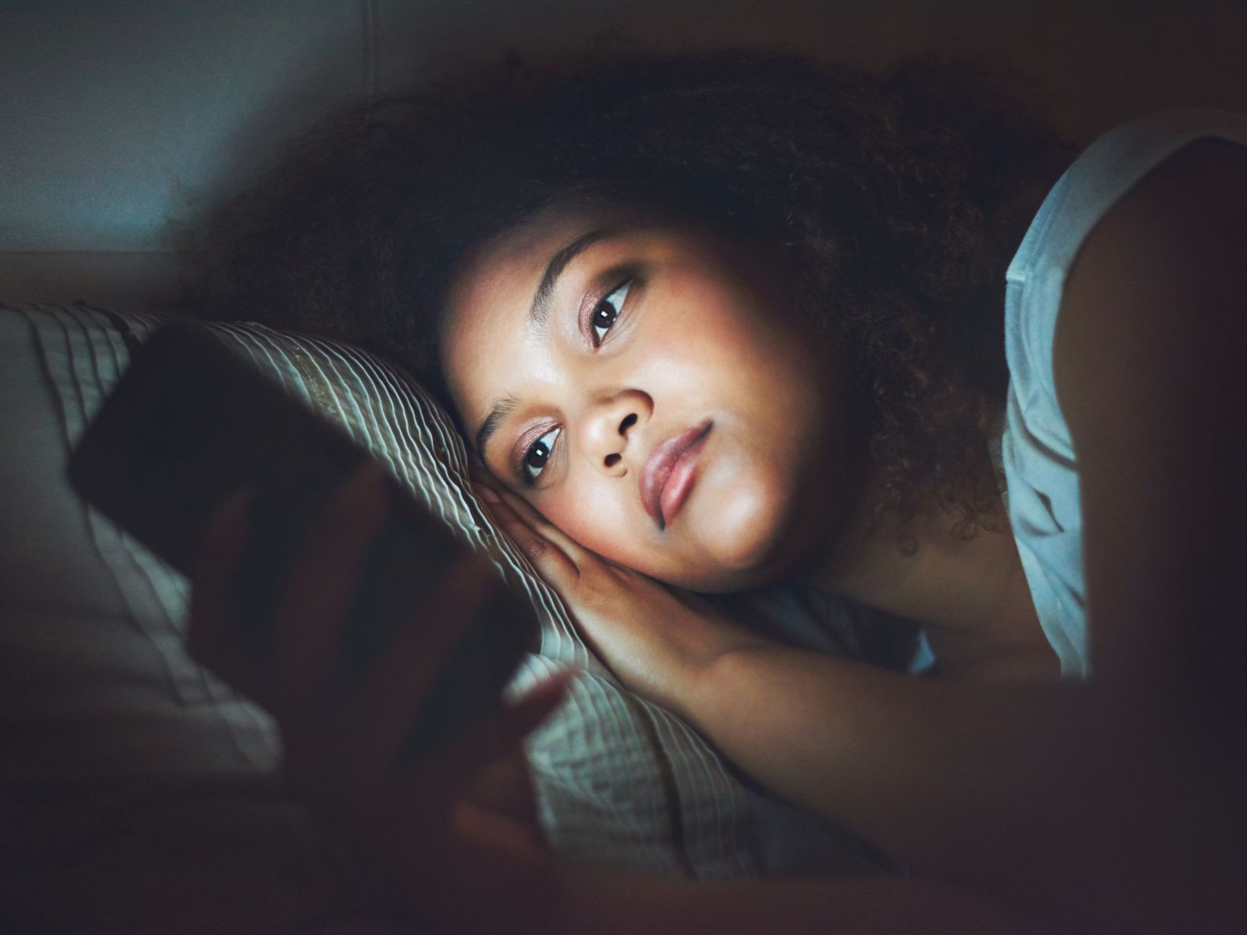 Shot of a young woman using a cellphone in bed at night