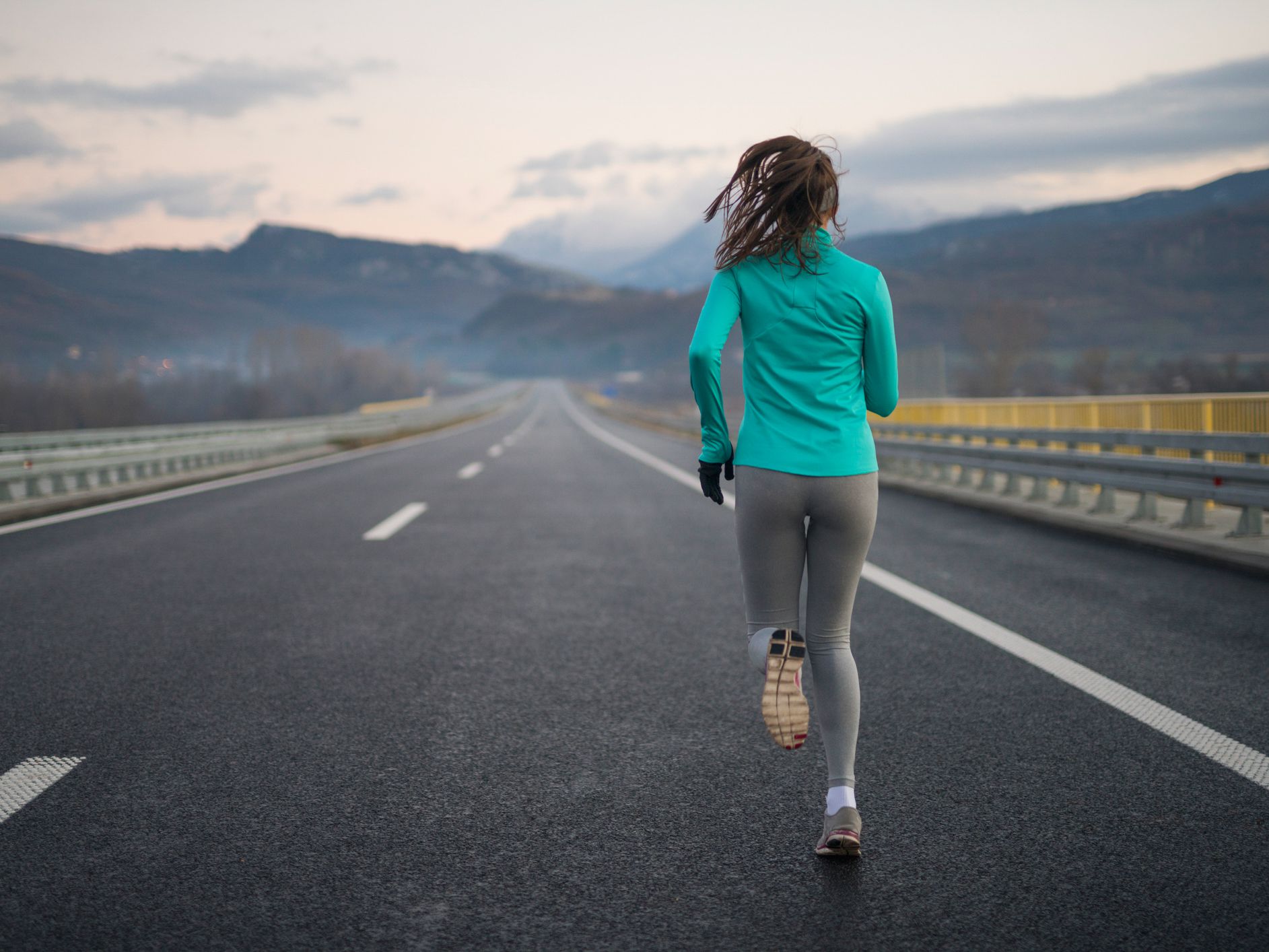 Rear view of a young female athlete running down the highway.