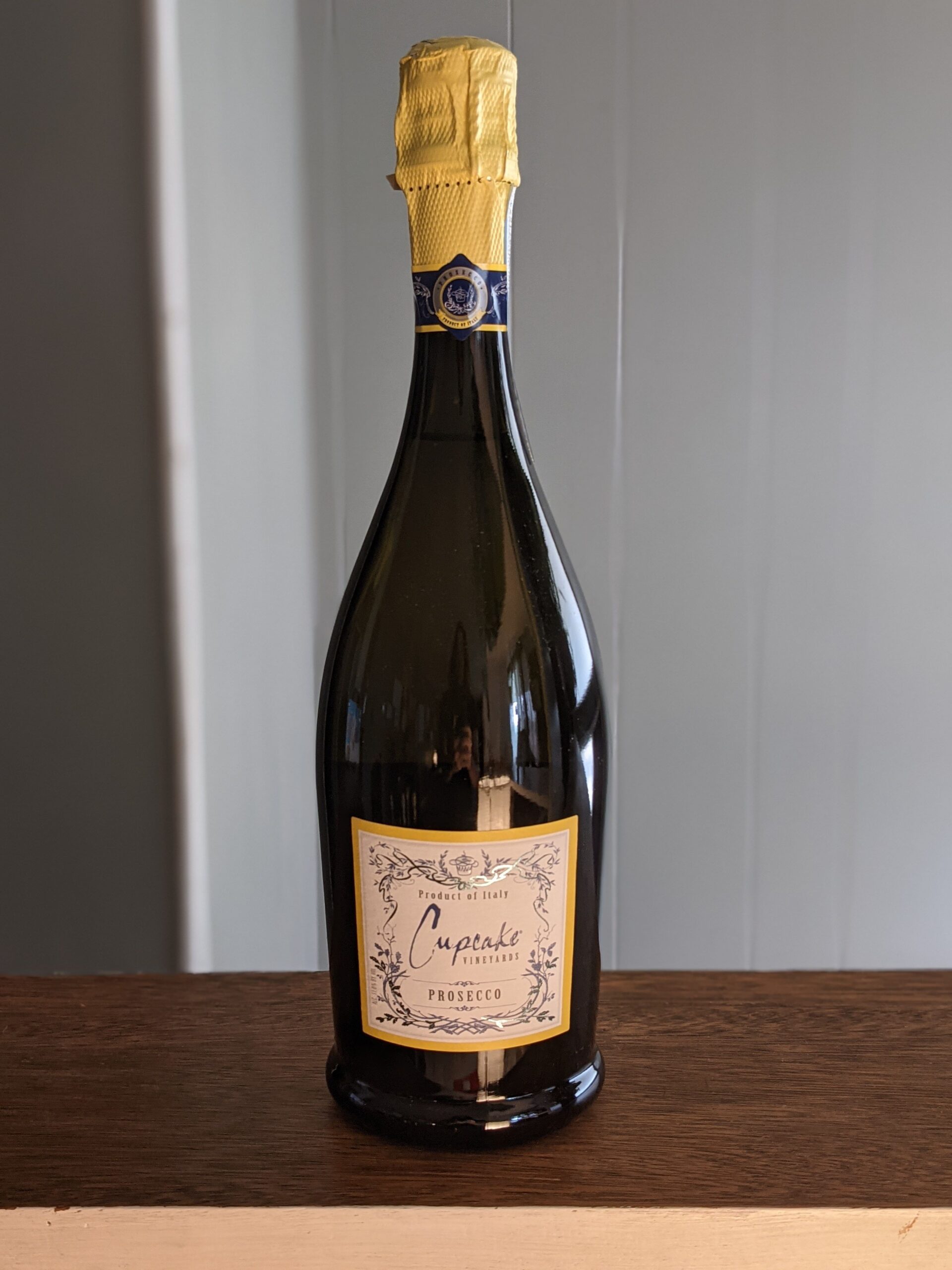 A sealed bottle of Cupcake Prosecco on a wooden ledge, white panel wooden wall blurred in the background