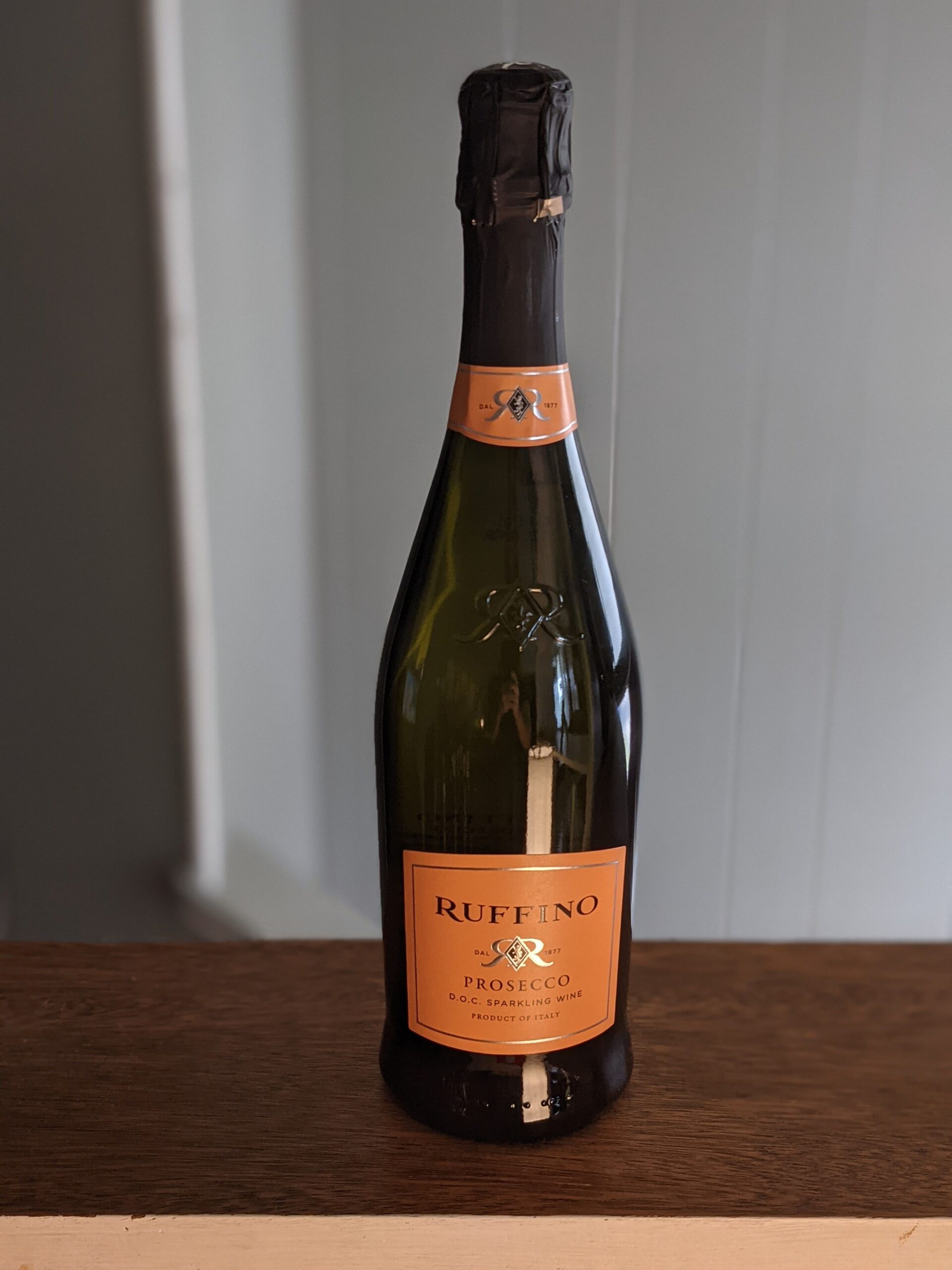 A sealed bottle of Ruffino Prosecco on a wooden ledge, white panel wooden wall blurred in the background