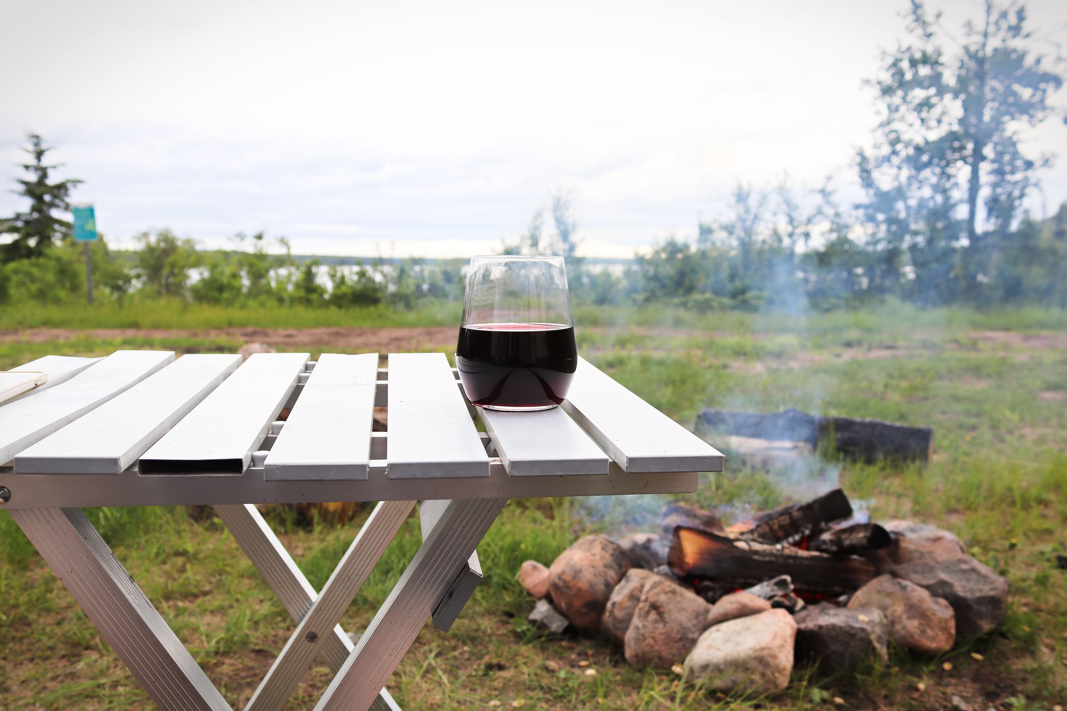 Picture of a wine glass with a lake and campfire in the background.