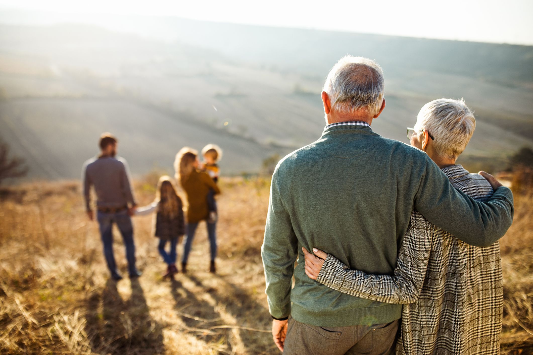embraced grandparents enjoying while looking at their family on a field in autumn day