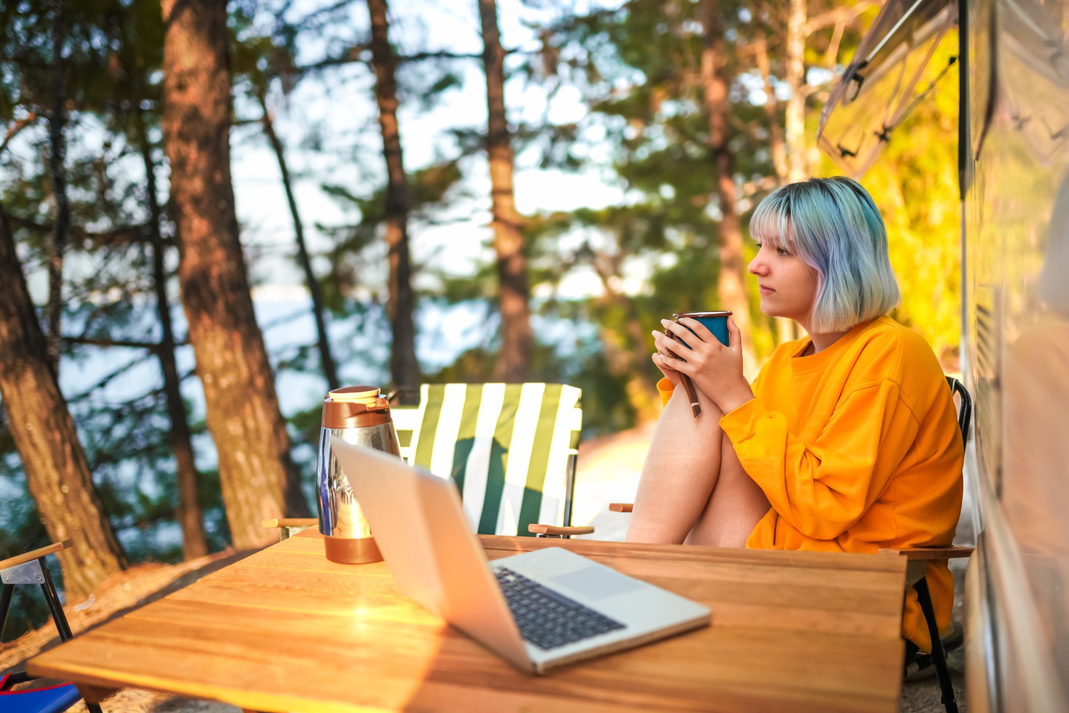 Young Woman using laptop while drinking coffee at camping