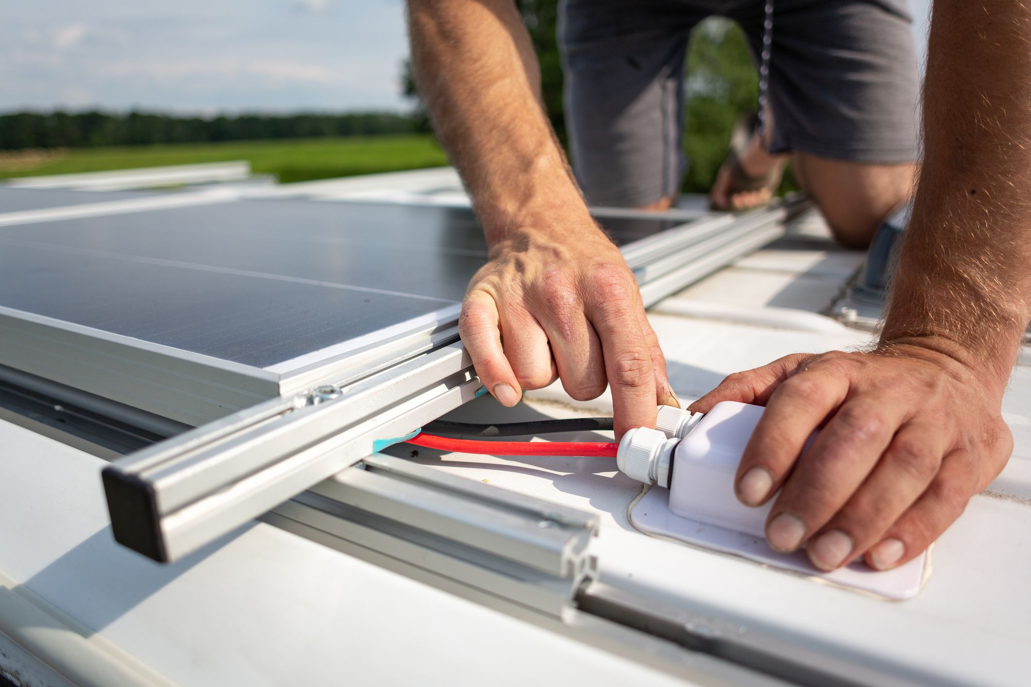 Close-up of hands connecting cables attached to solar panels on top of a camper van.