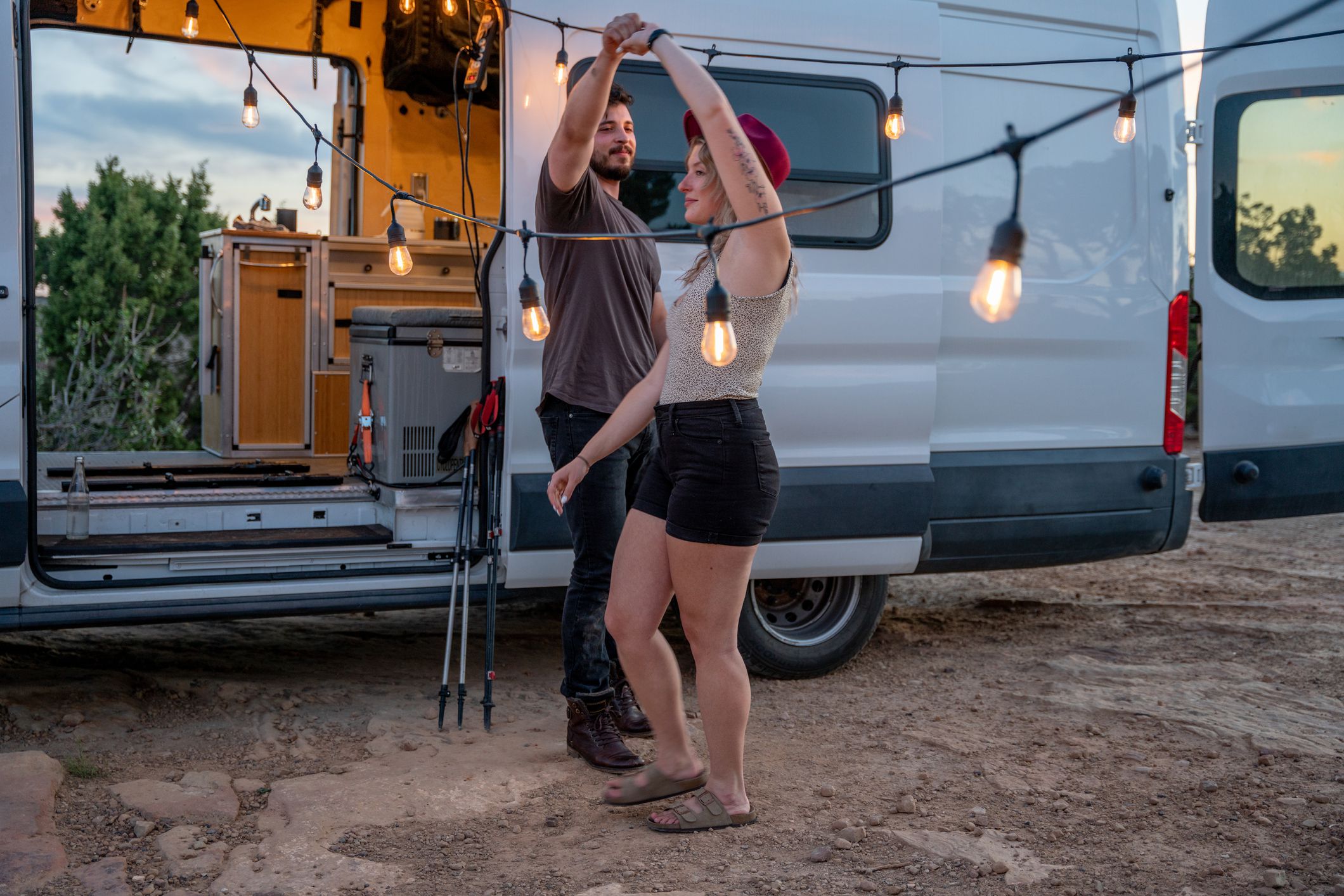 Happy Couple Romantically Dancing together at a glamping van life campsite in a desert at dusk