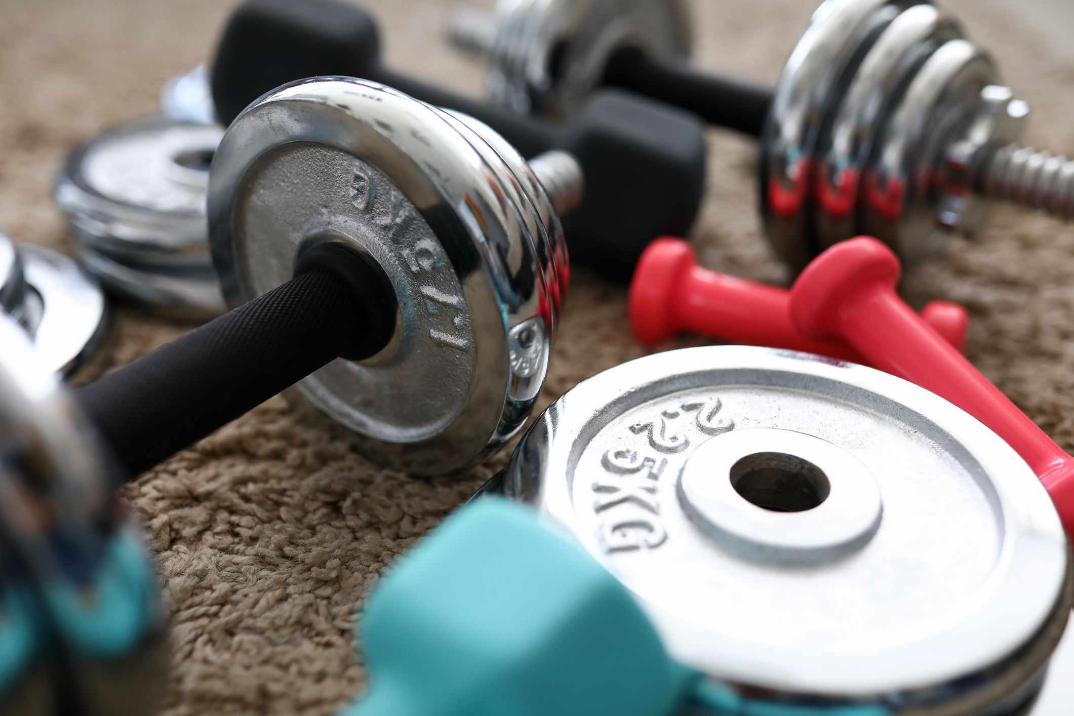 Pile of shiny chrome dumbbells disks lying around grip at home rug as domestic sport exercises during coronavirus quarantine period close-up