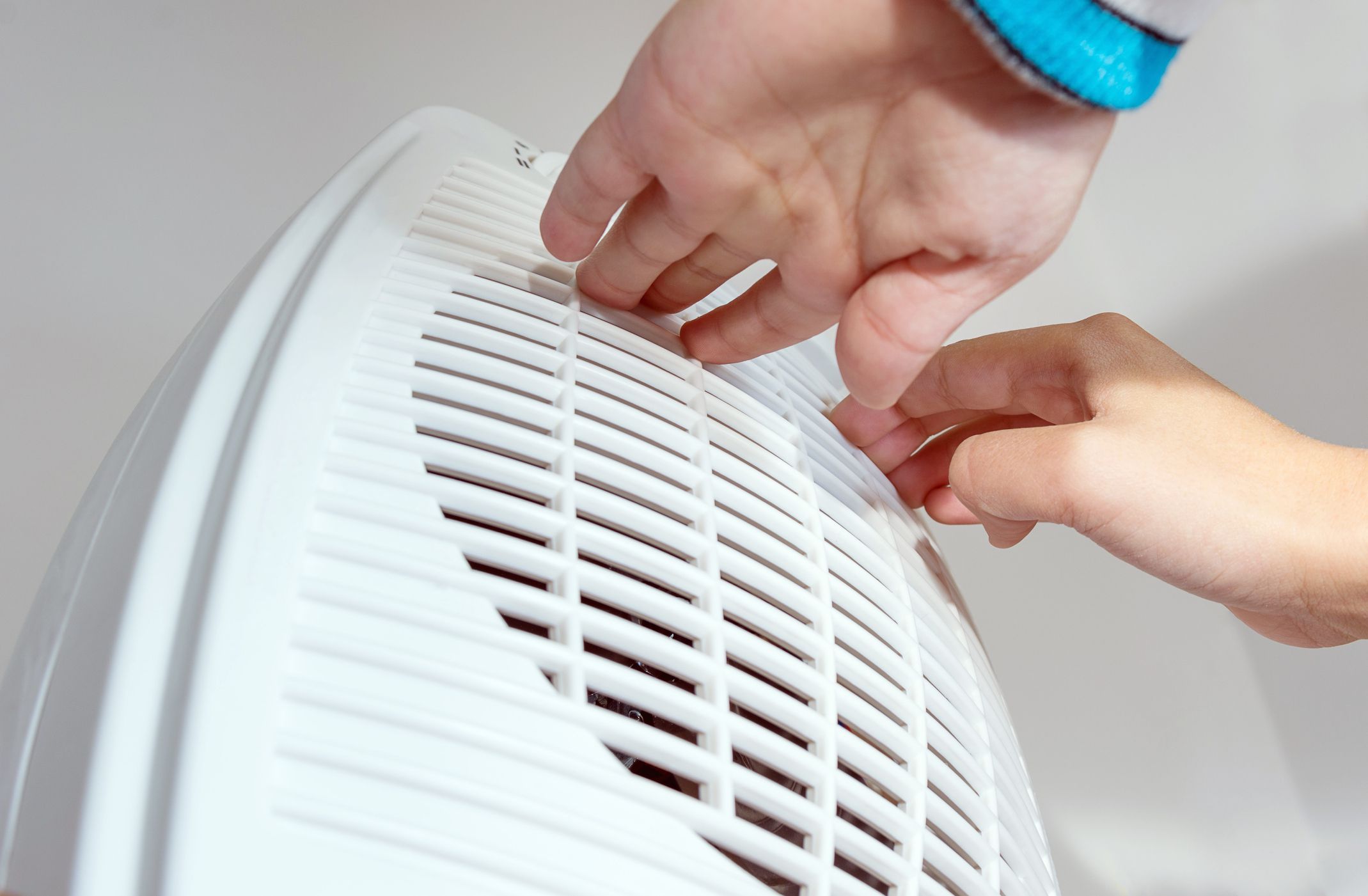 Young boy warming cold hands in front of electric heating radiator in winter time. Electric fan heater at home. Part of body, selective focus.