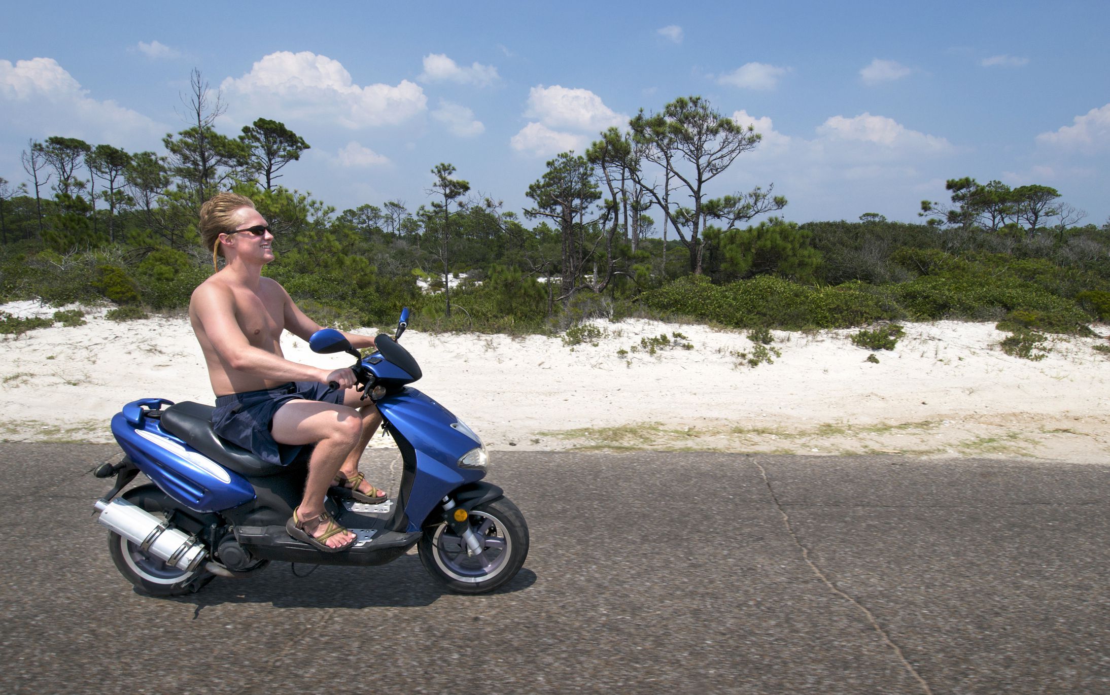Young man rides a scooter on a road through a beach/park in Florida.