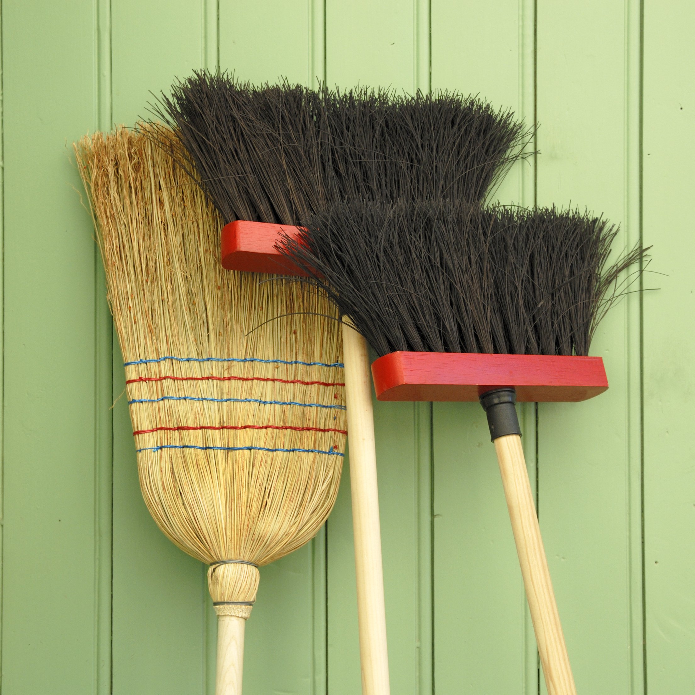 collection of brooms against a green wall