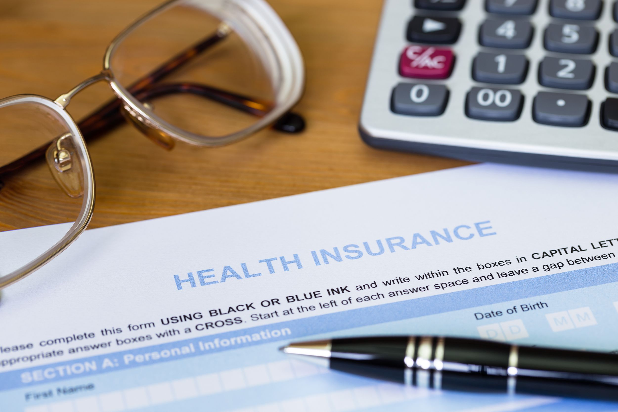 health insurance application form with pen, calculator, and glasses