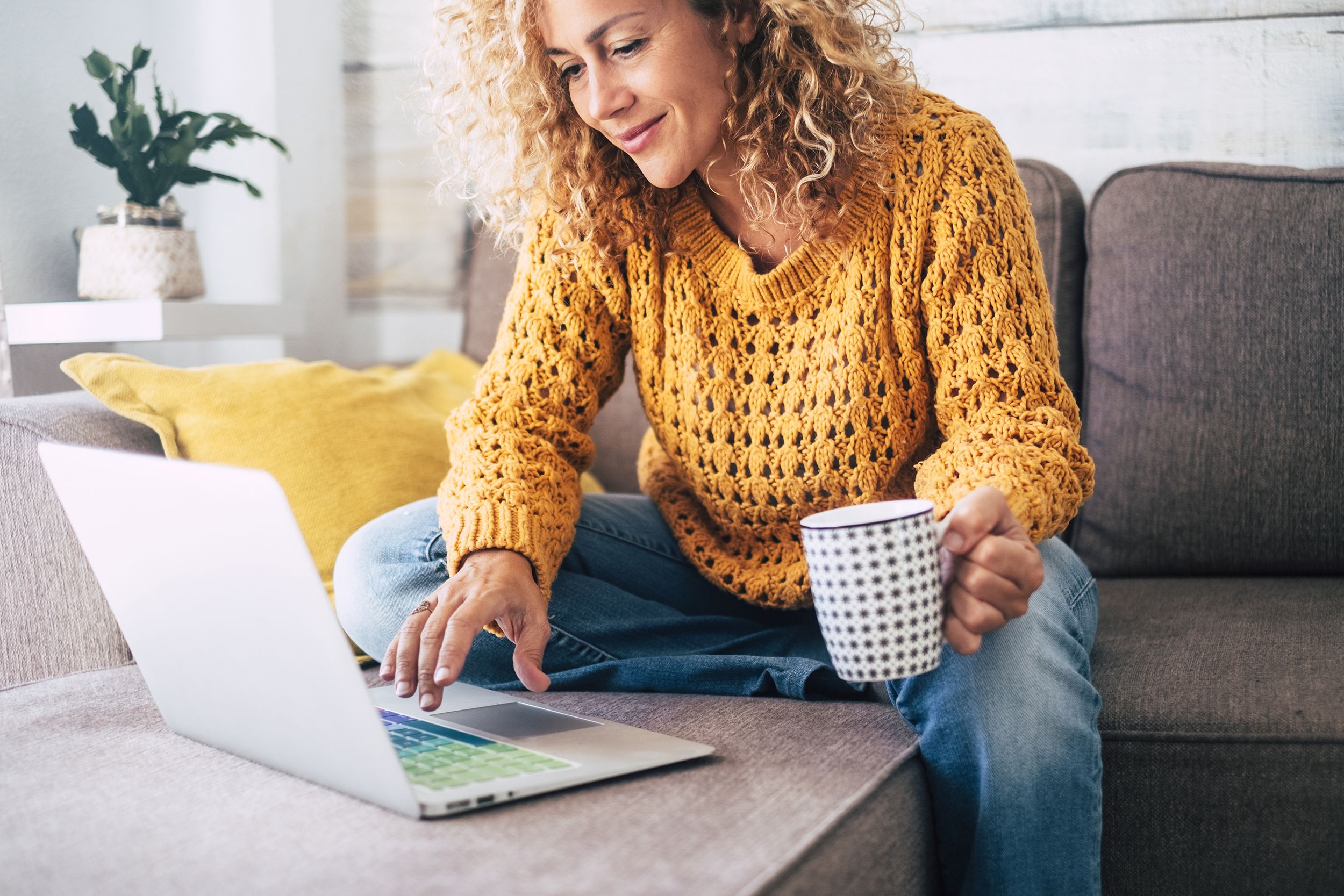 woman working at a laptop, sitting down on the sofa at home