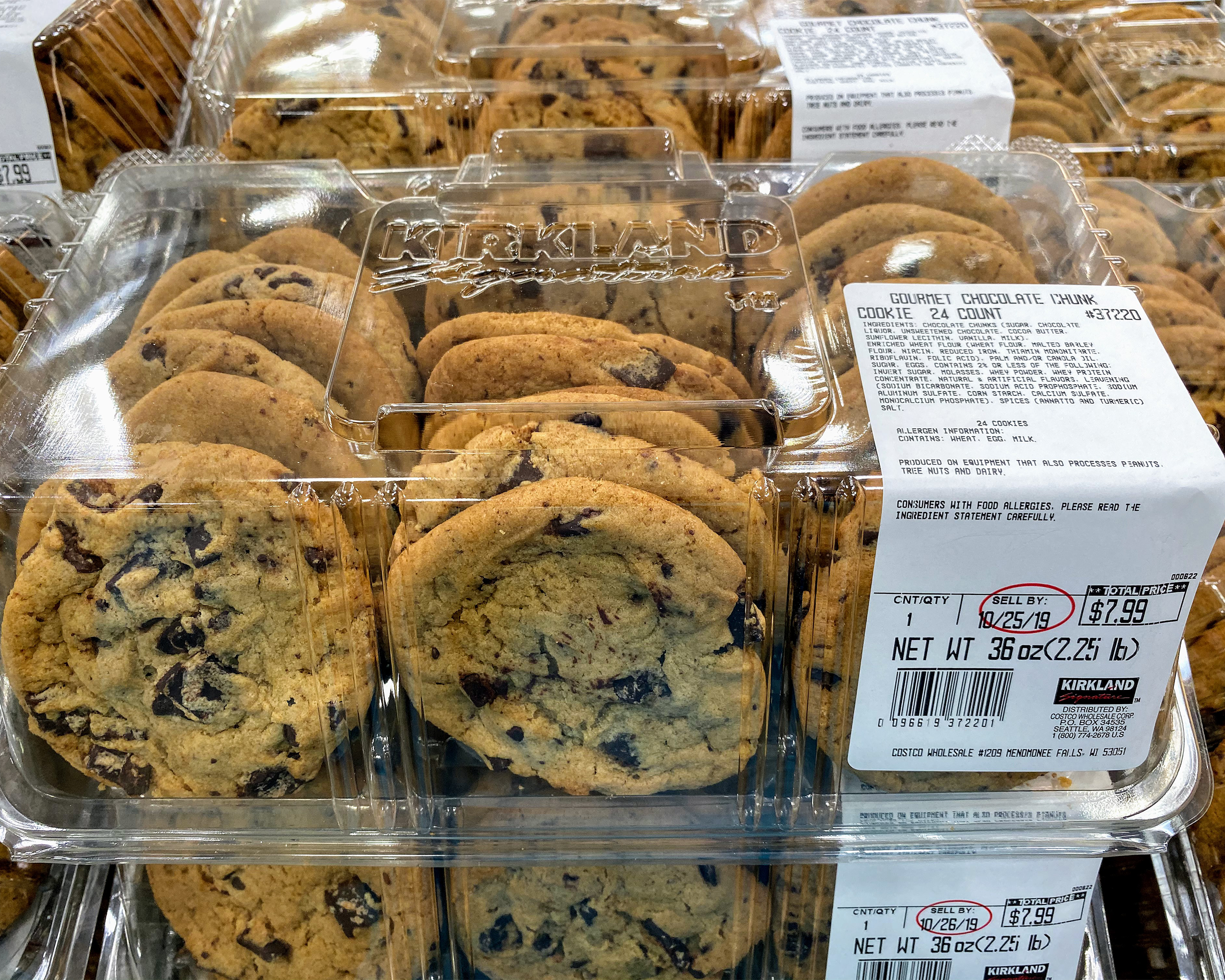 Closeup of Kirkland Gourmet Chocolate Chunk Cookies at a Costco, 24 cookies in three rows in a plastic container, several stacks of these cookies