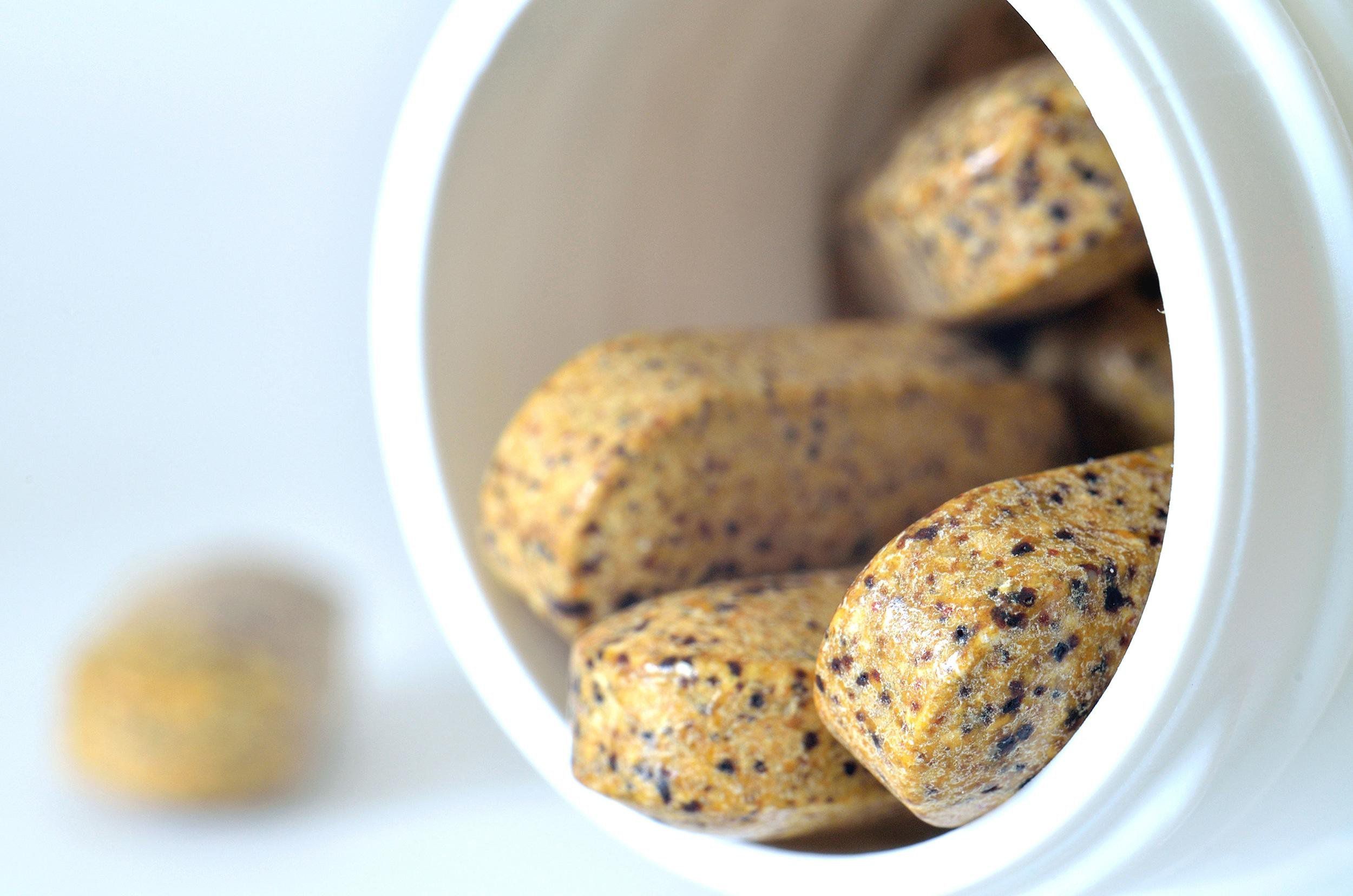 Closeup of bottle opening with a few multivitamin supplement pills hanging around the edge with a blurred background of light blue and one multivitamin Supplement pill