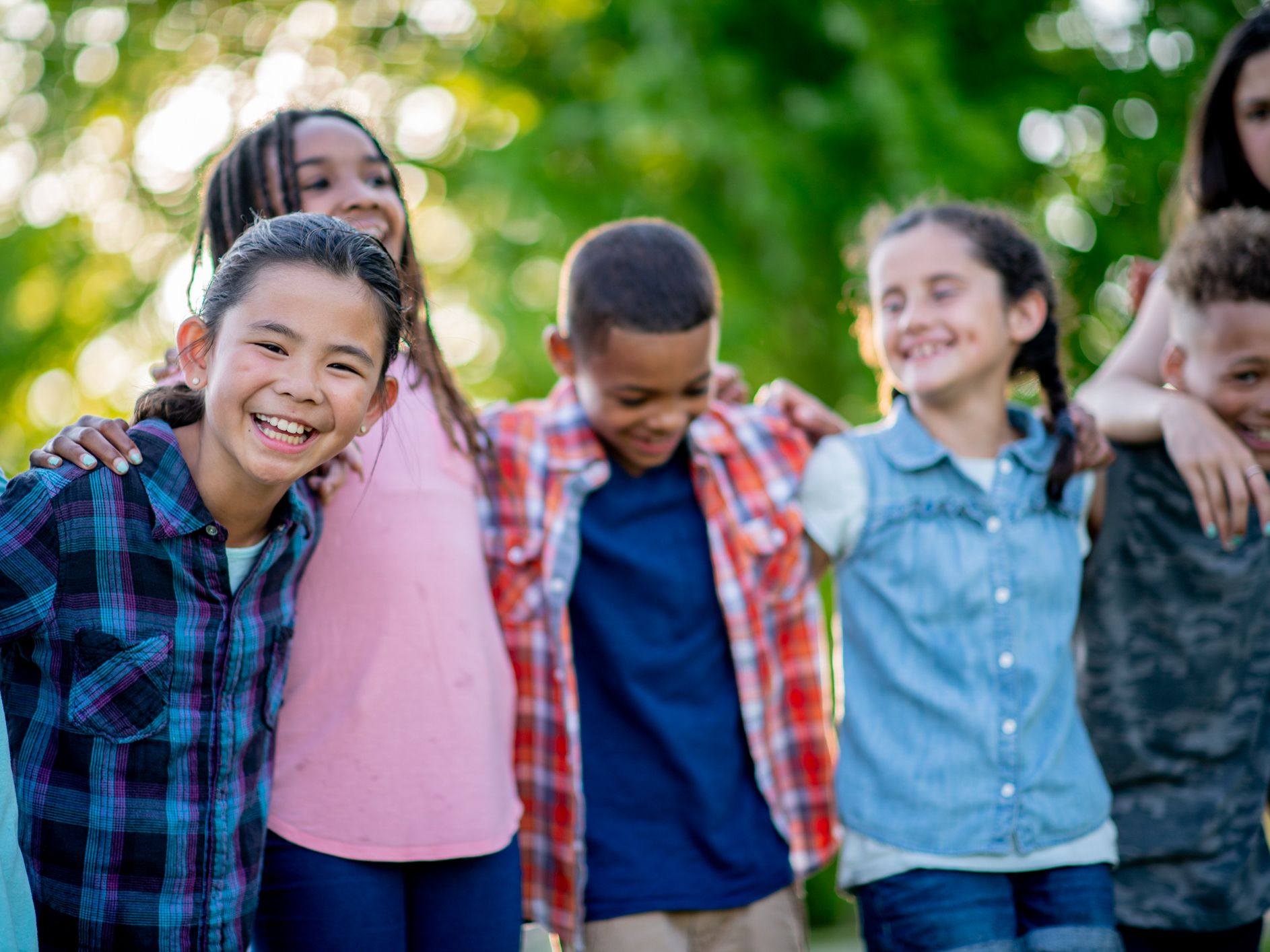 A group of elementary kids are outdoors in the open. They are standing in a group and smiling.