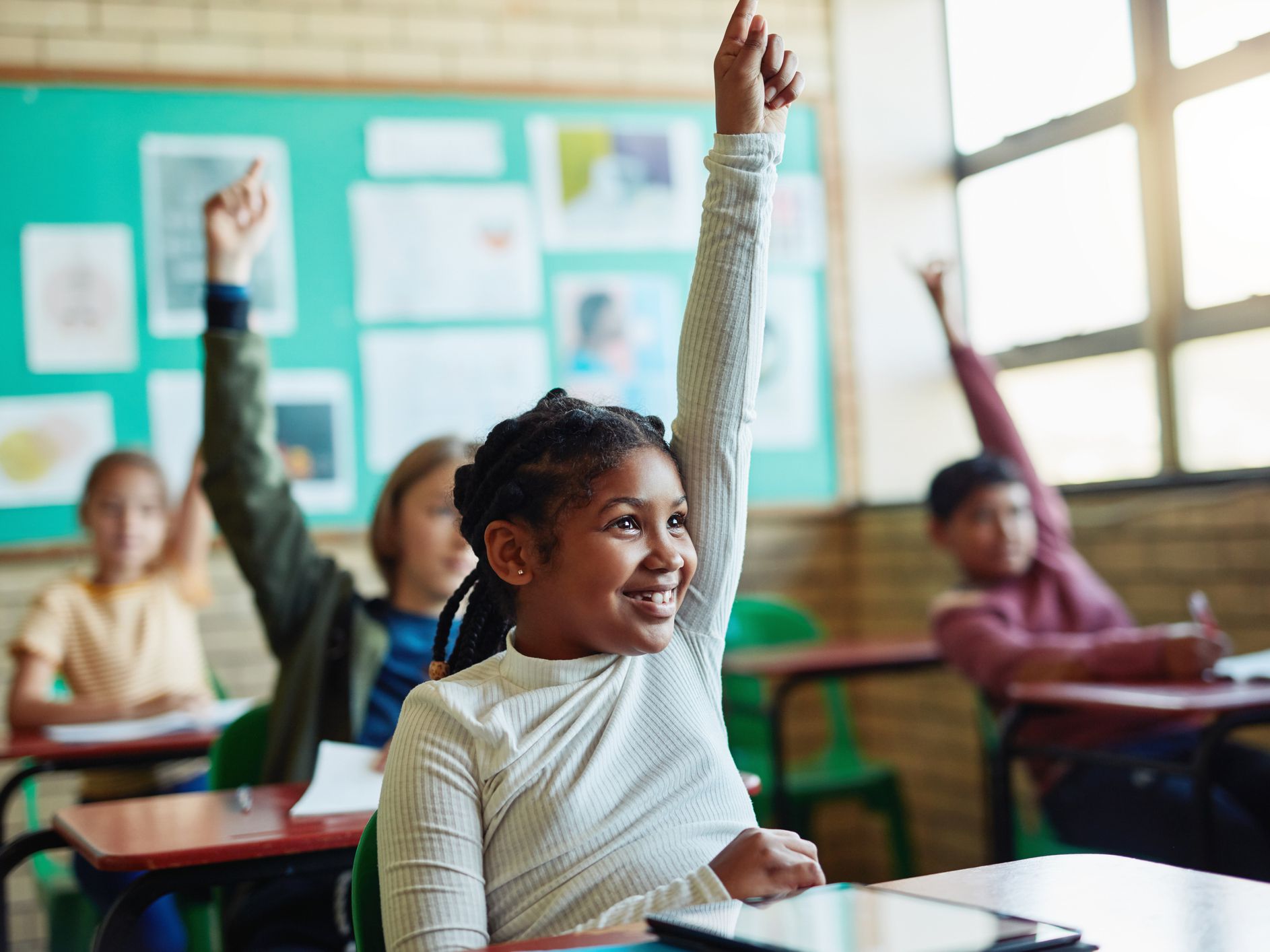 Shot of young children raising their hands in a classroom