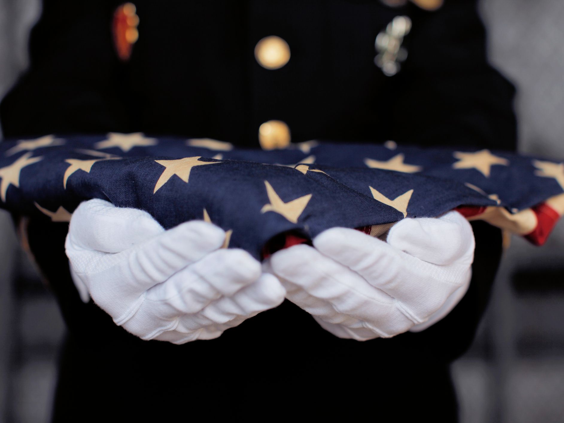 Military personnel holding a folded US flag.