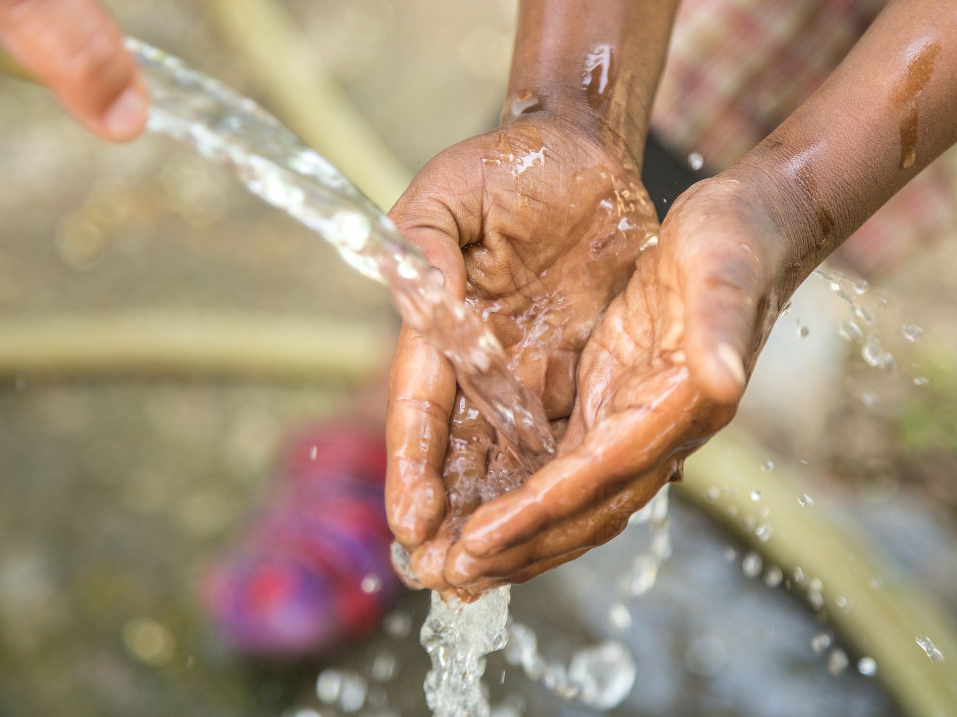 The hands of a child from a poor community are outstretched to receive a flowing stream of clear, fresh water.