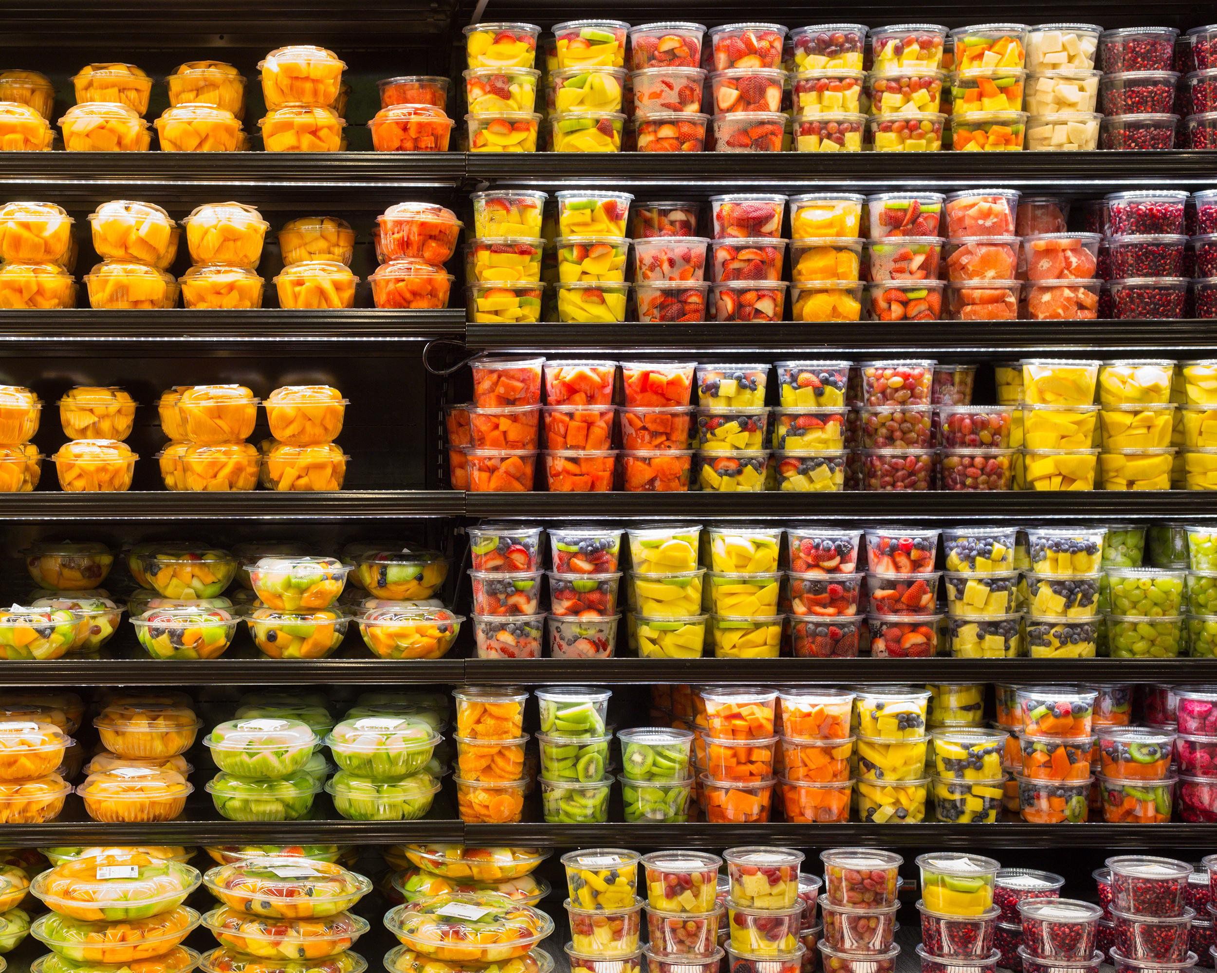 Six rows of a selection of packaged cut fruits in the refrigerated area at a grocery store, very colorful, black shelves