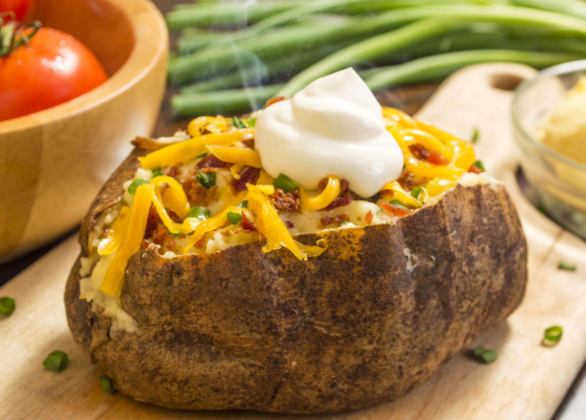 Baked potato with chives, black pepper and sour cream on a white plate.