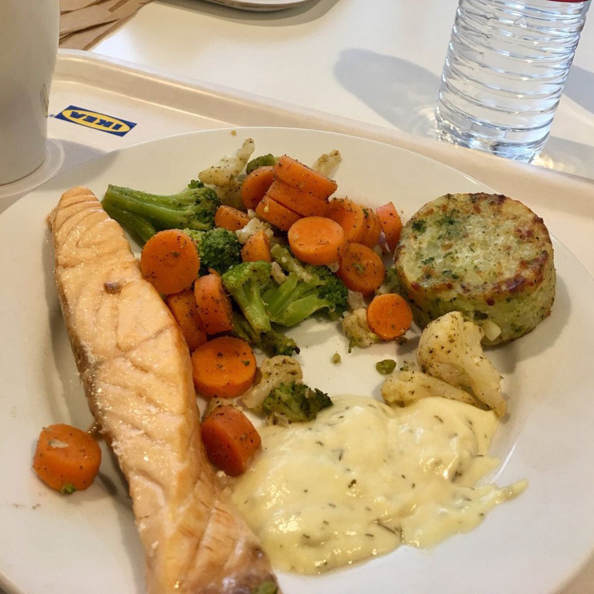 Salmon fillet with mashed potatoes, cabbage, fennel, capers, and roasted buckwheat on plate at Ikea Restaurant with water bottle in background