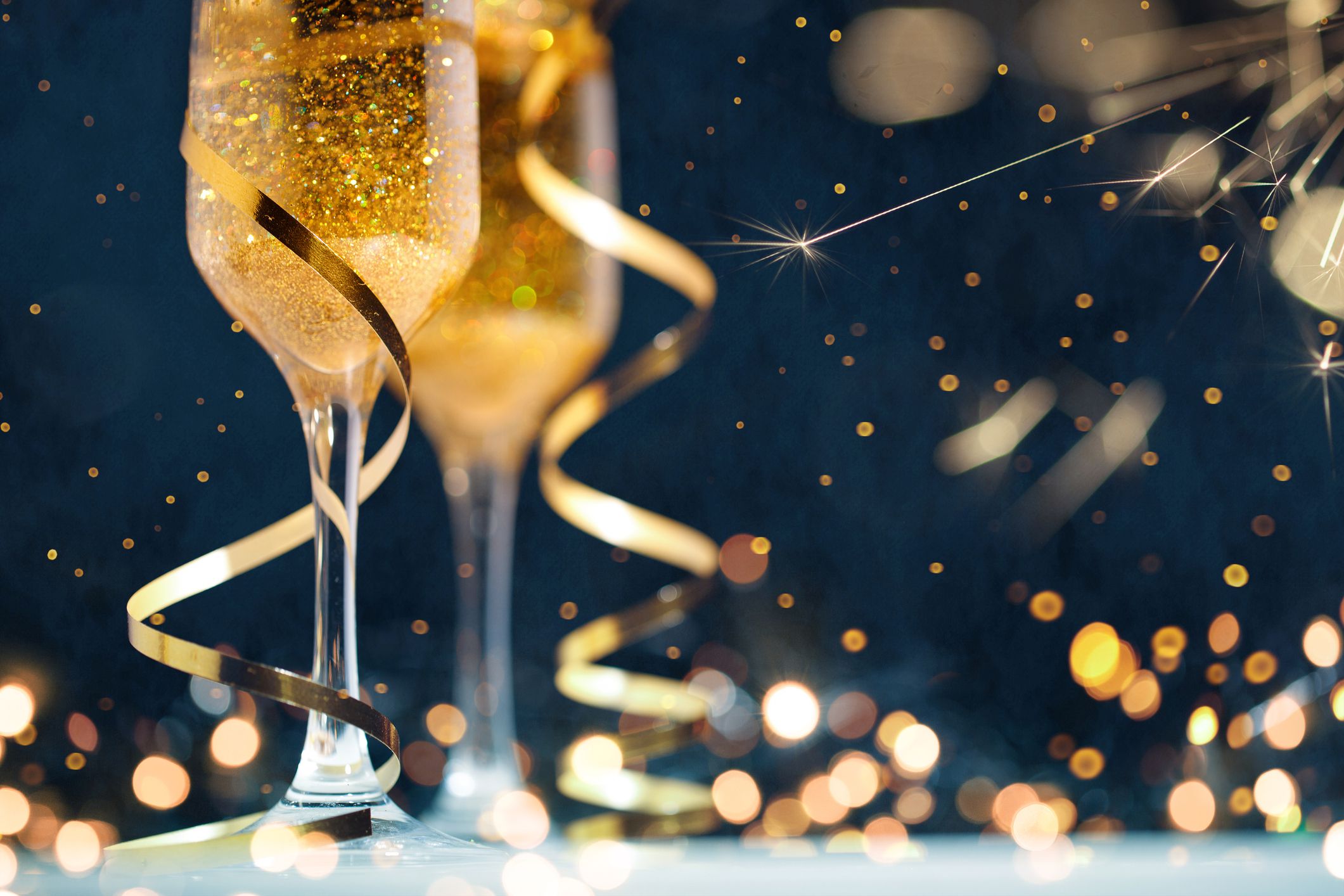 Two glasses of champagne with golden confetti, glitter, serpentine and lights. Night of celebration concept