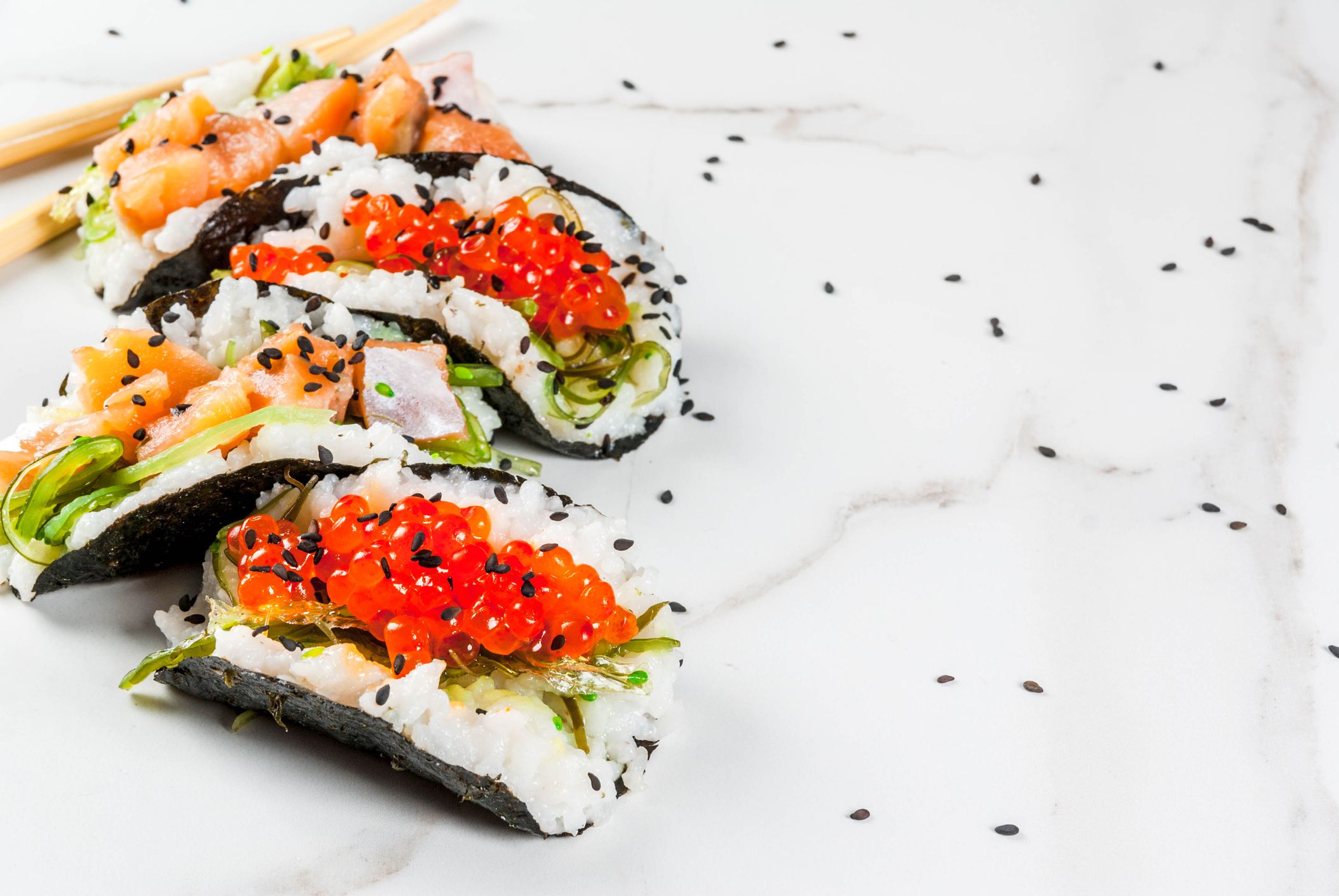 Trend hybrid food. Japanese Asian cuisine. Mini sushi-tacos, sandwiches with salmon, hayashi wakame, daikon, ginger, red caviar. White marble table, with chopsticks, soy sauce. Copy space