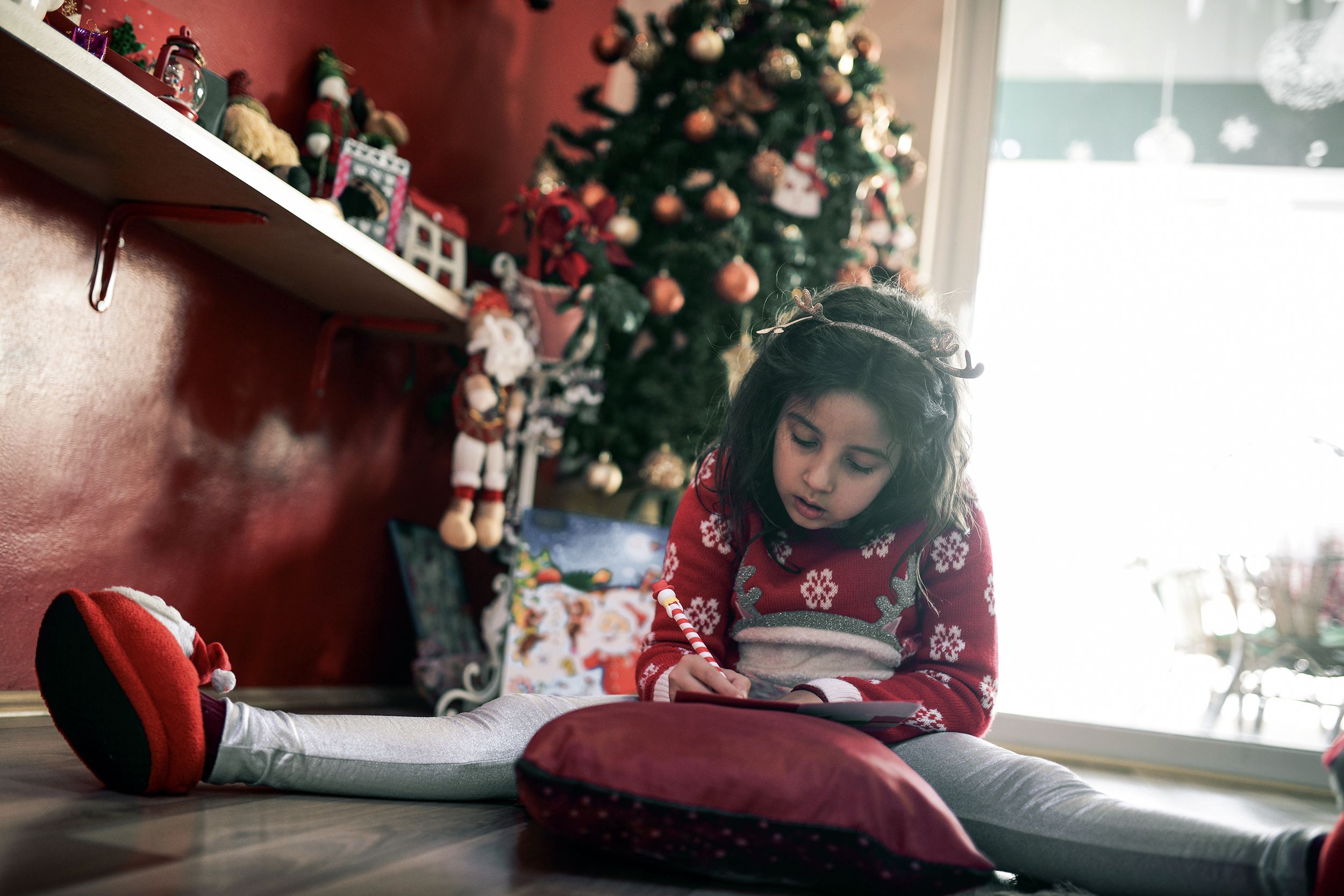 little girl writing her wishes on letter to santa under Christmas tree