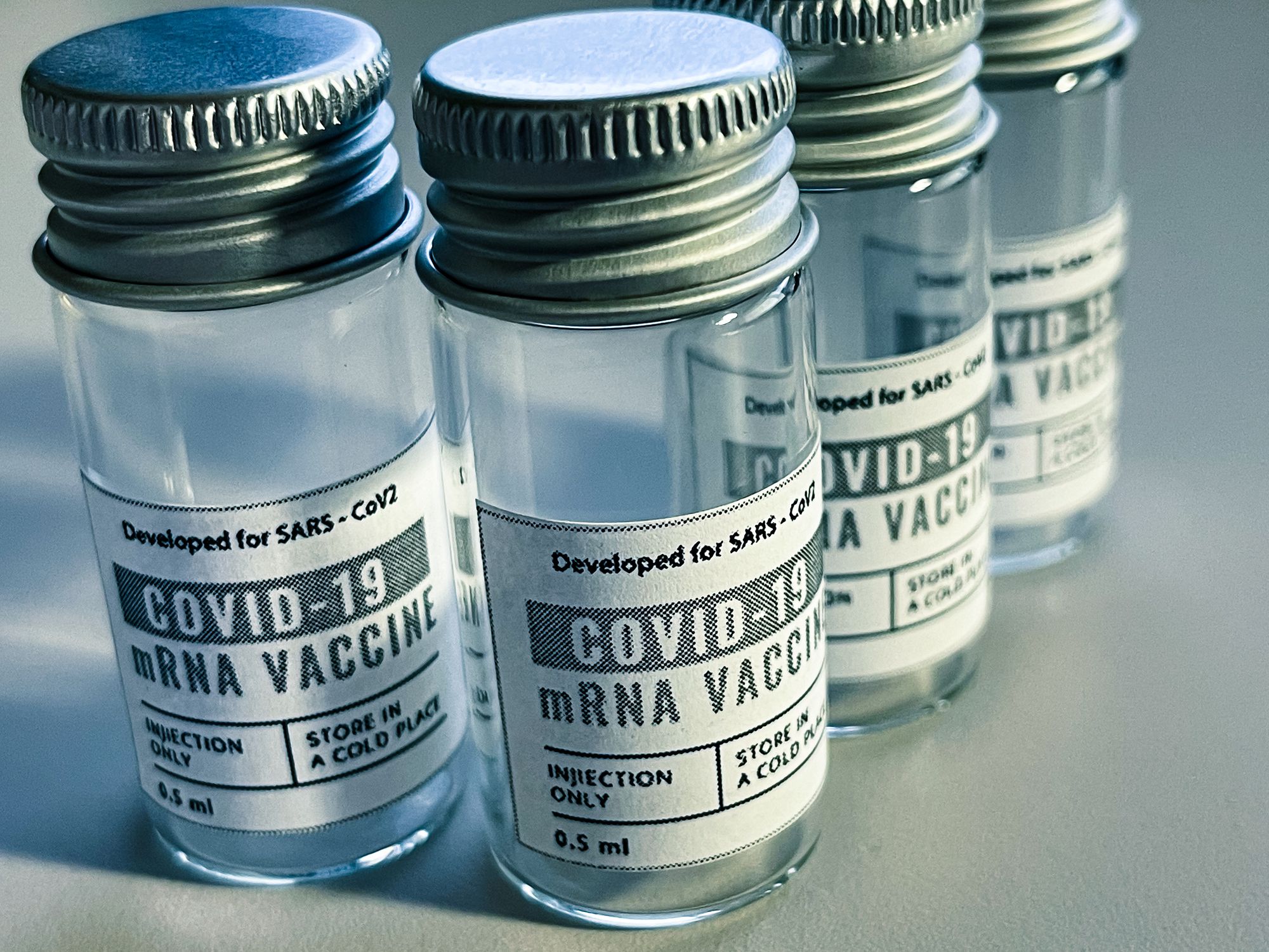 Closeup of four COVID-19 vaccine vials, two closeup and two in line after second closeup one, on grey background