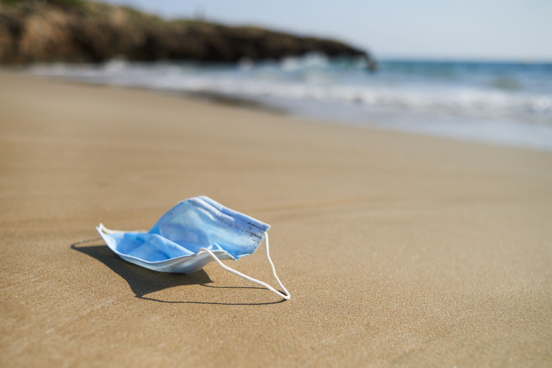 Closeup of a blue used surgical mask on the wet sand of the seashore of a lonely beach during COVID-19
