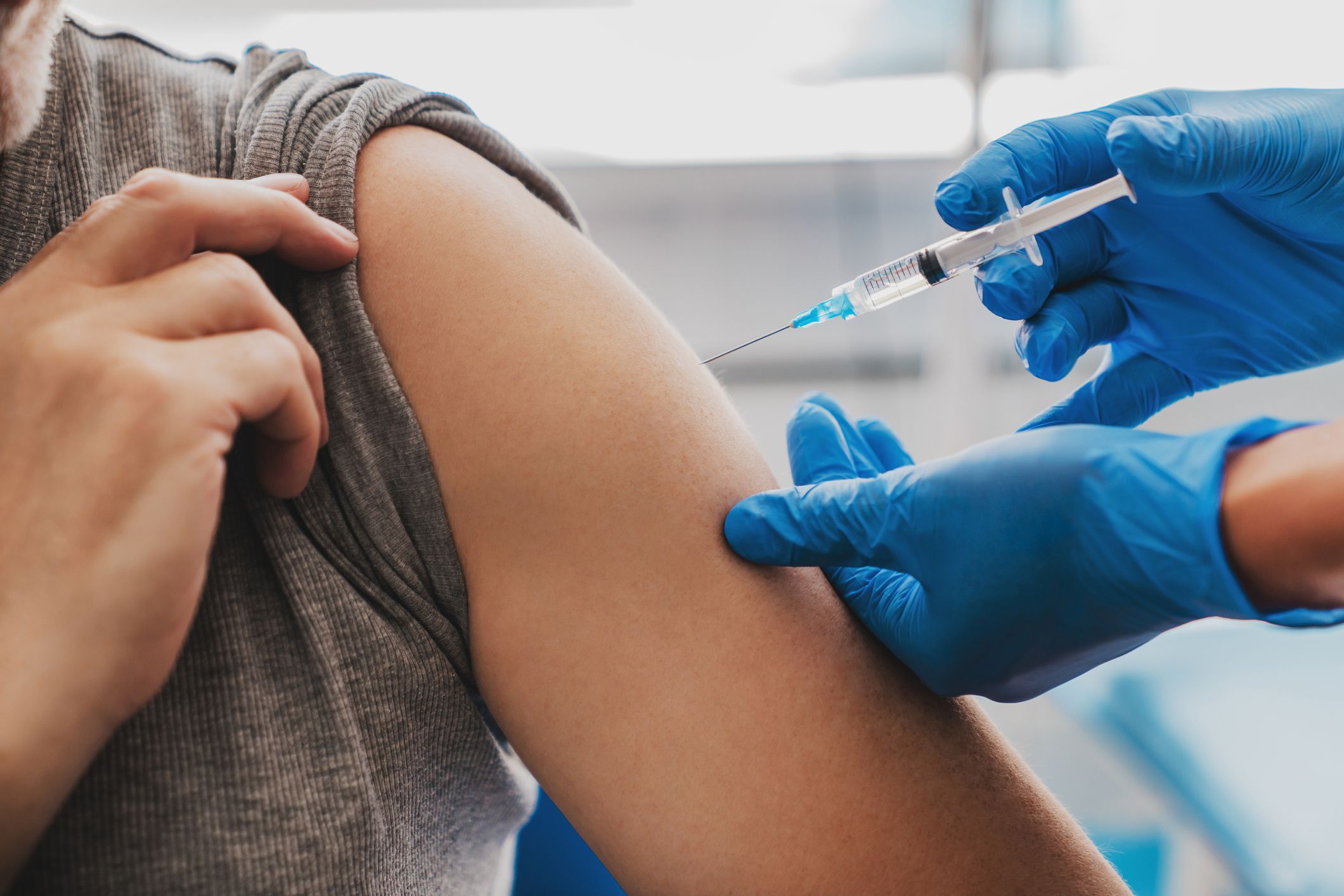Male adult receiving COVID-19 vaccination from two blue gloved hands in healthcare setting with blurred background