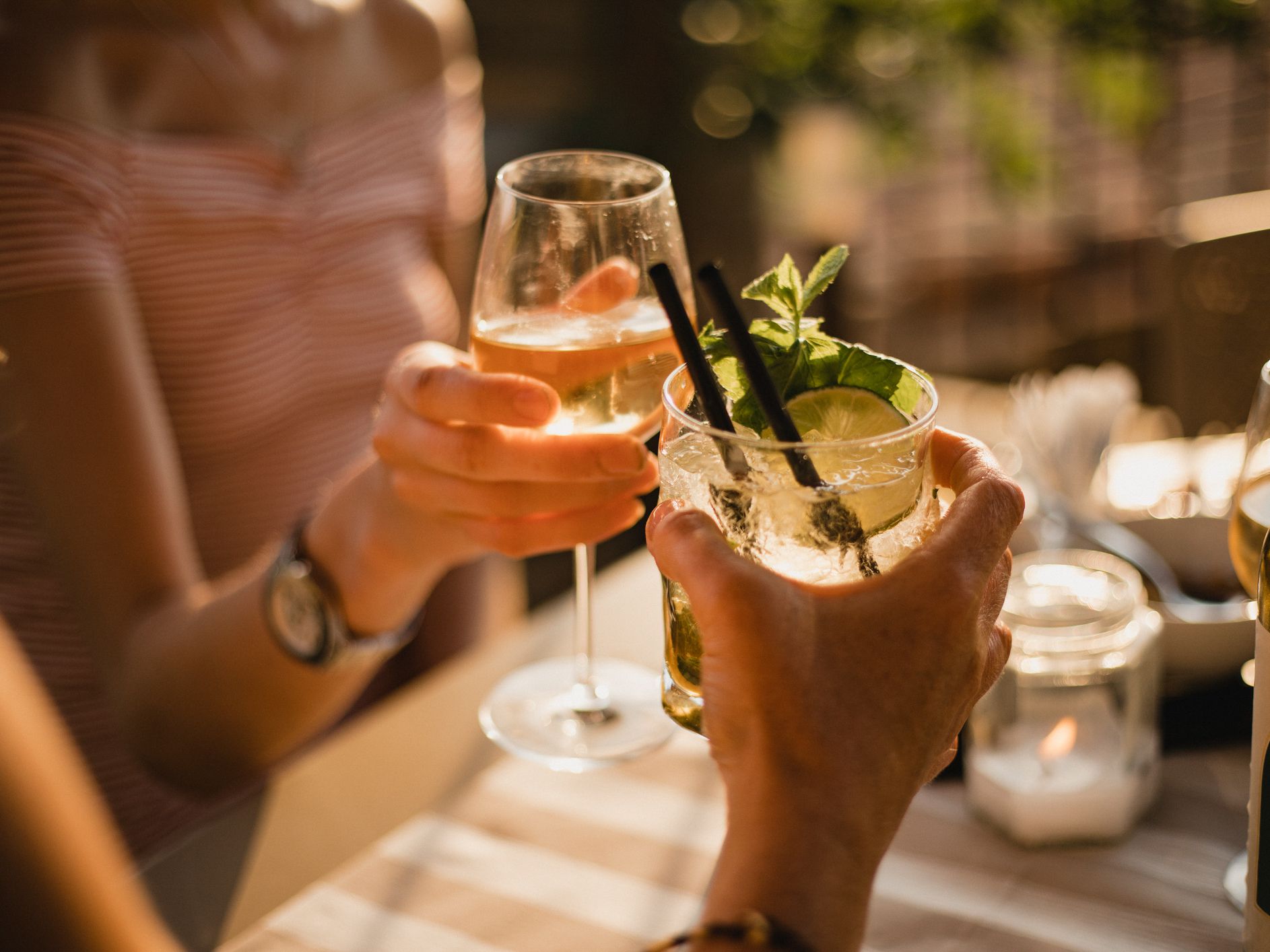 Two unrecognisable people sitting down at a table during sunset, they are making a celebratory