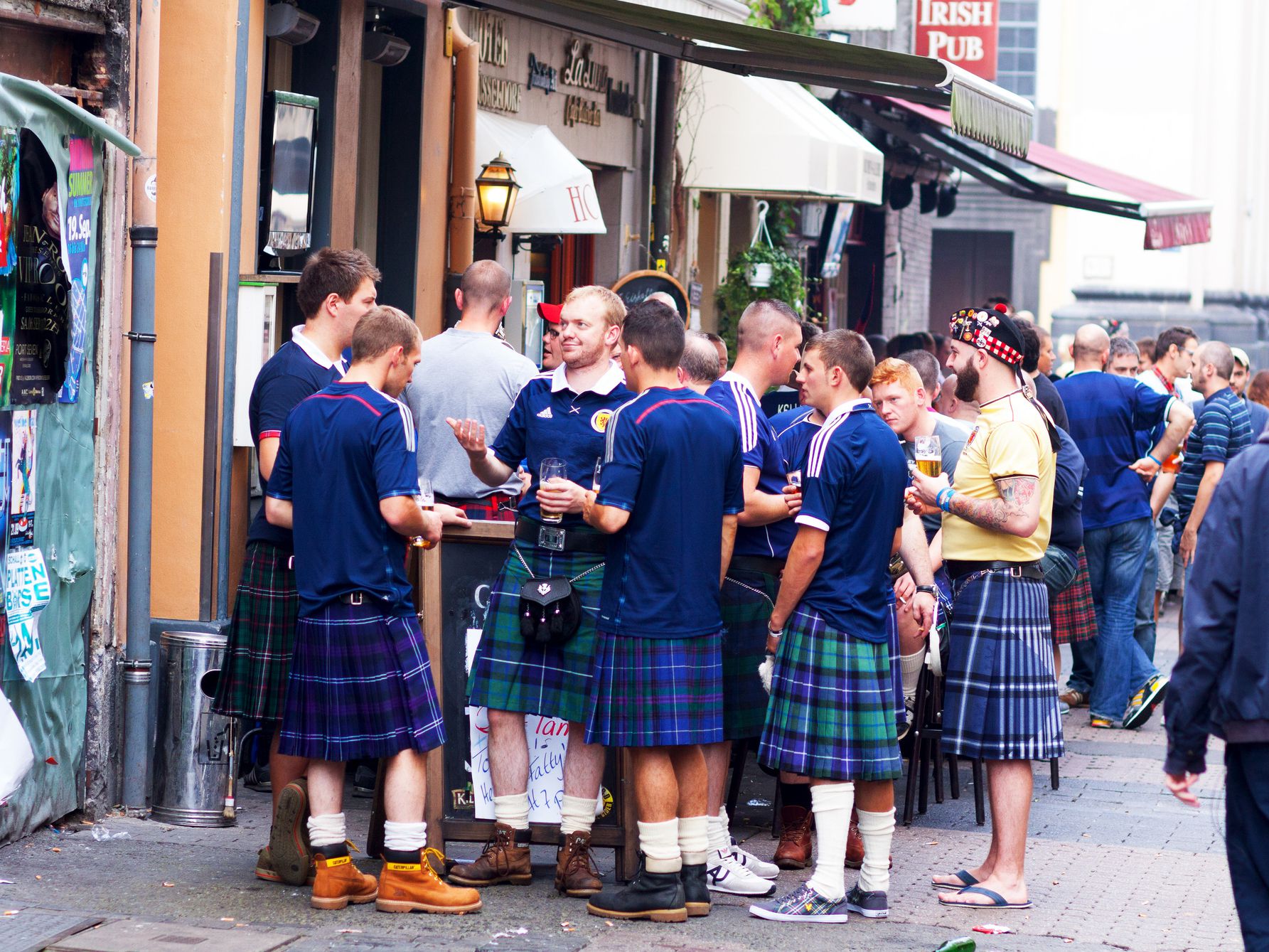 A group of Scosmen wearing kilts is standing outside of bar in Altstadt of Düsseldorf in summer. Guys are fans of Scottish football team and are visiting Düsseldorf for European Champiognship qualifikation match between Germany and Düsseldorf. Men are dri