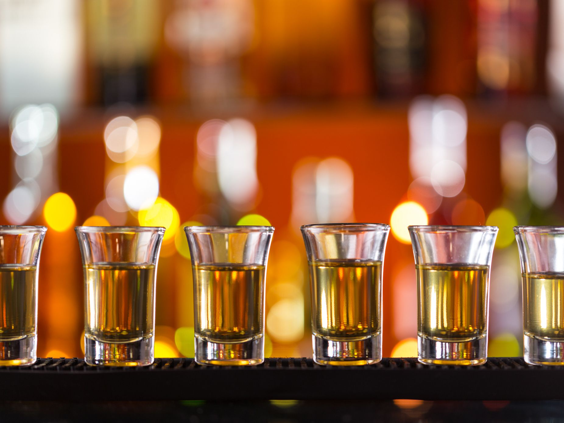 Variation of hard alcoholic shots served on bar counter. Blur bottles on background