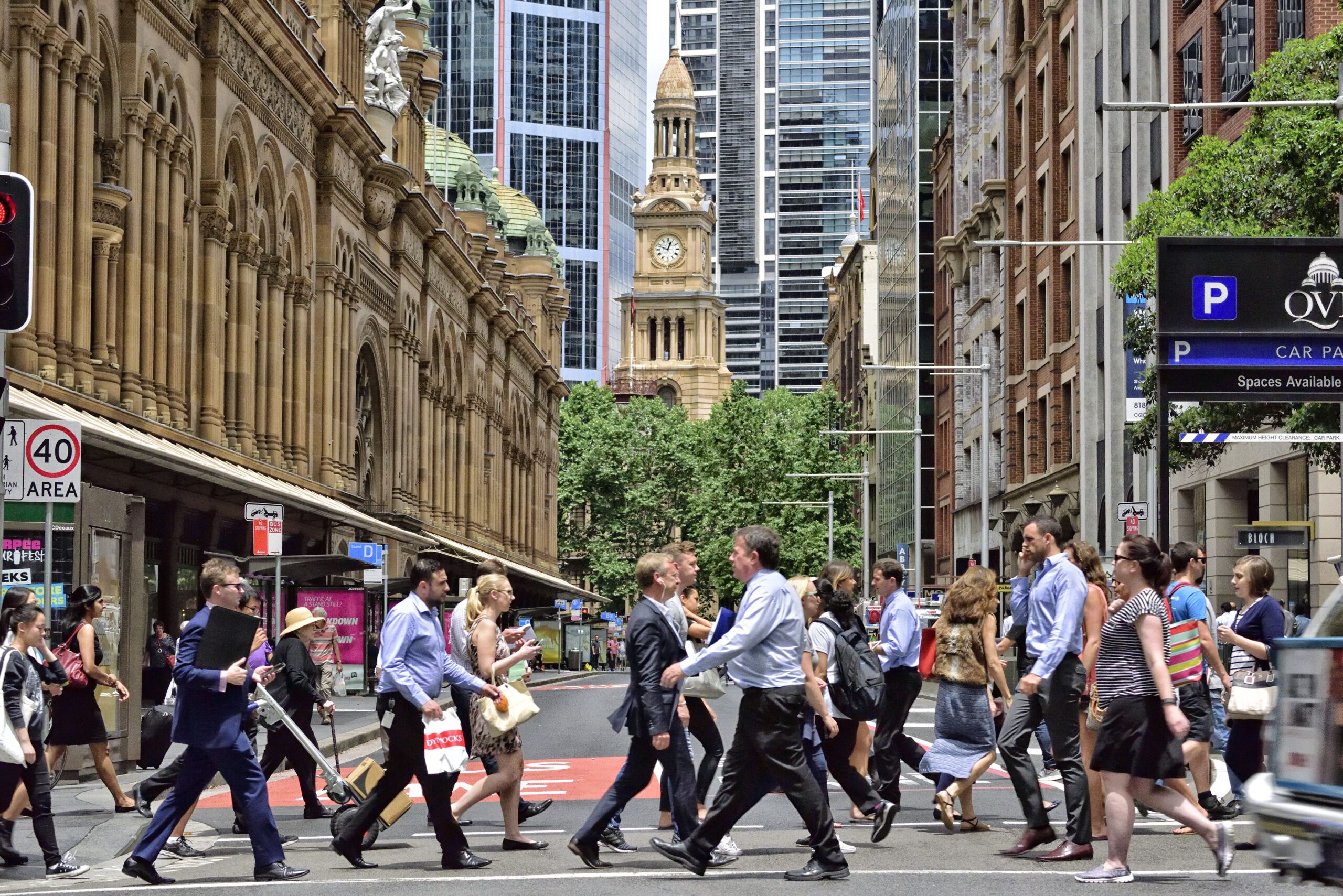 People crowd crossing street in central Sydney, Australia, landmark in background, shopping center to the left