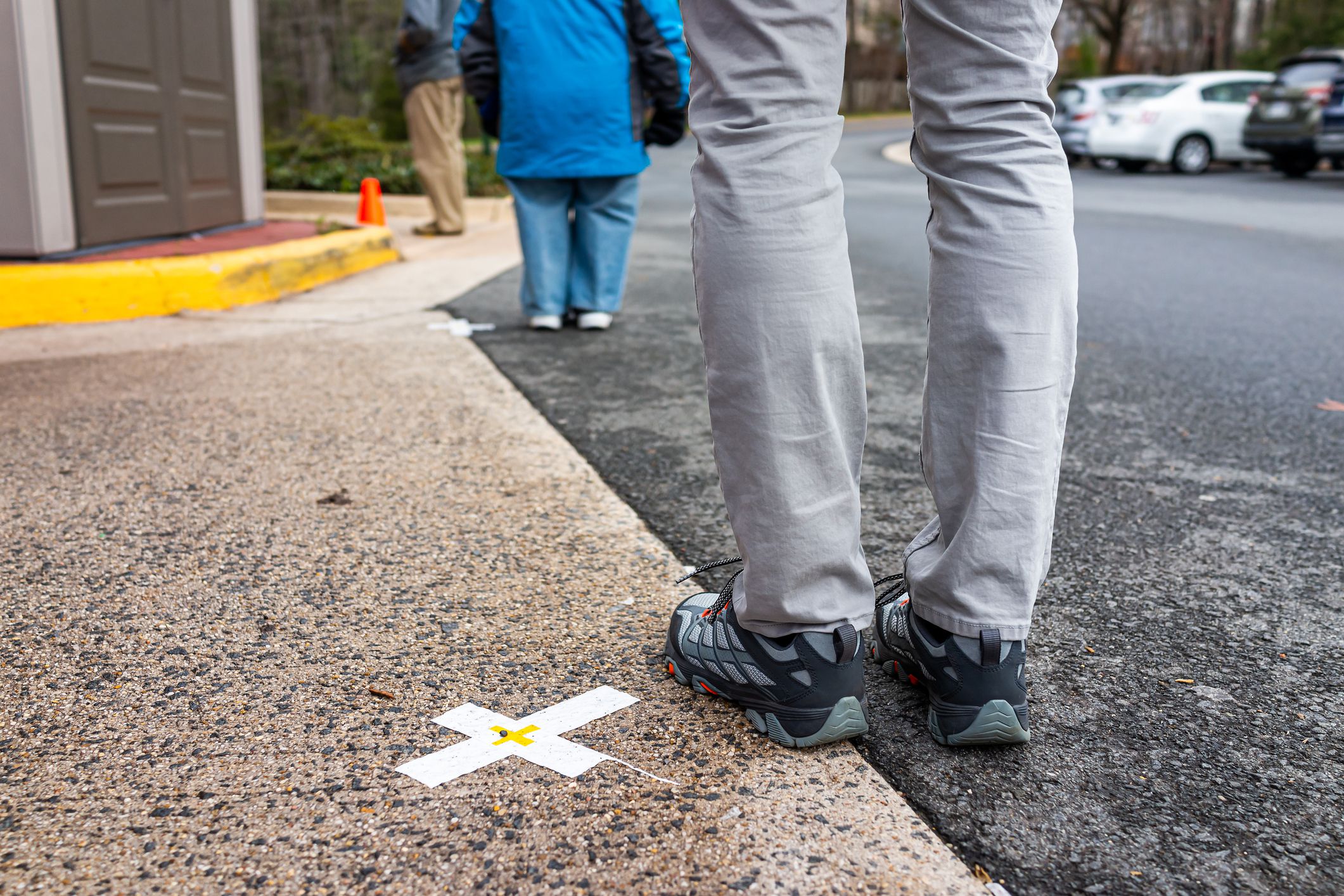 People standing waiting in line far apart to maintain social distancing during COVID-19 with mark cross signs on sidewalk pavement by grocery food store