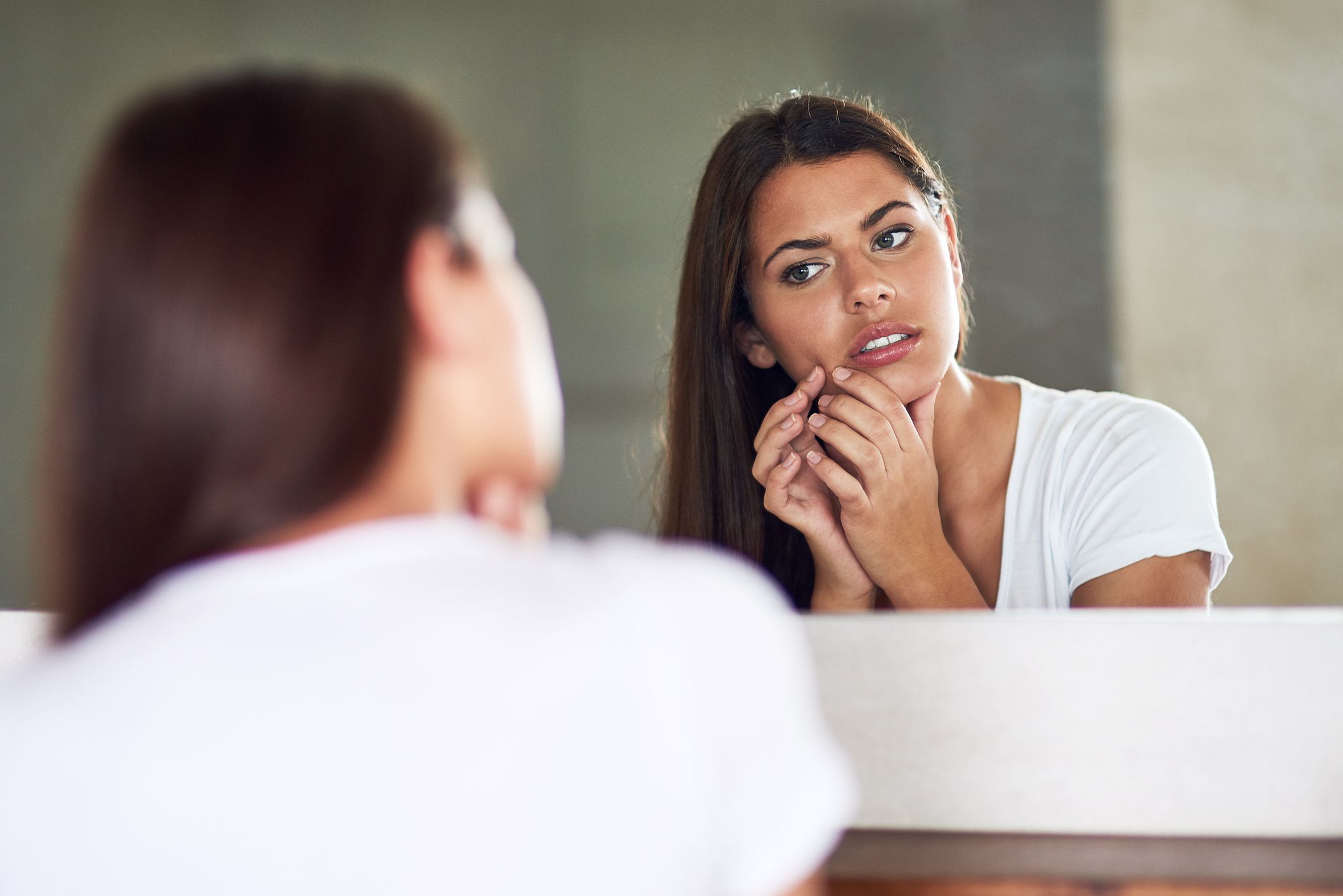 Frowning young woman examining an imperfection on her skin in the mirror at home