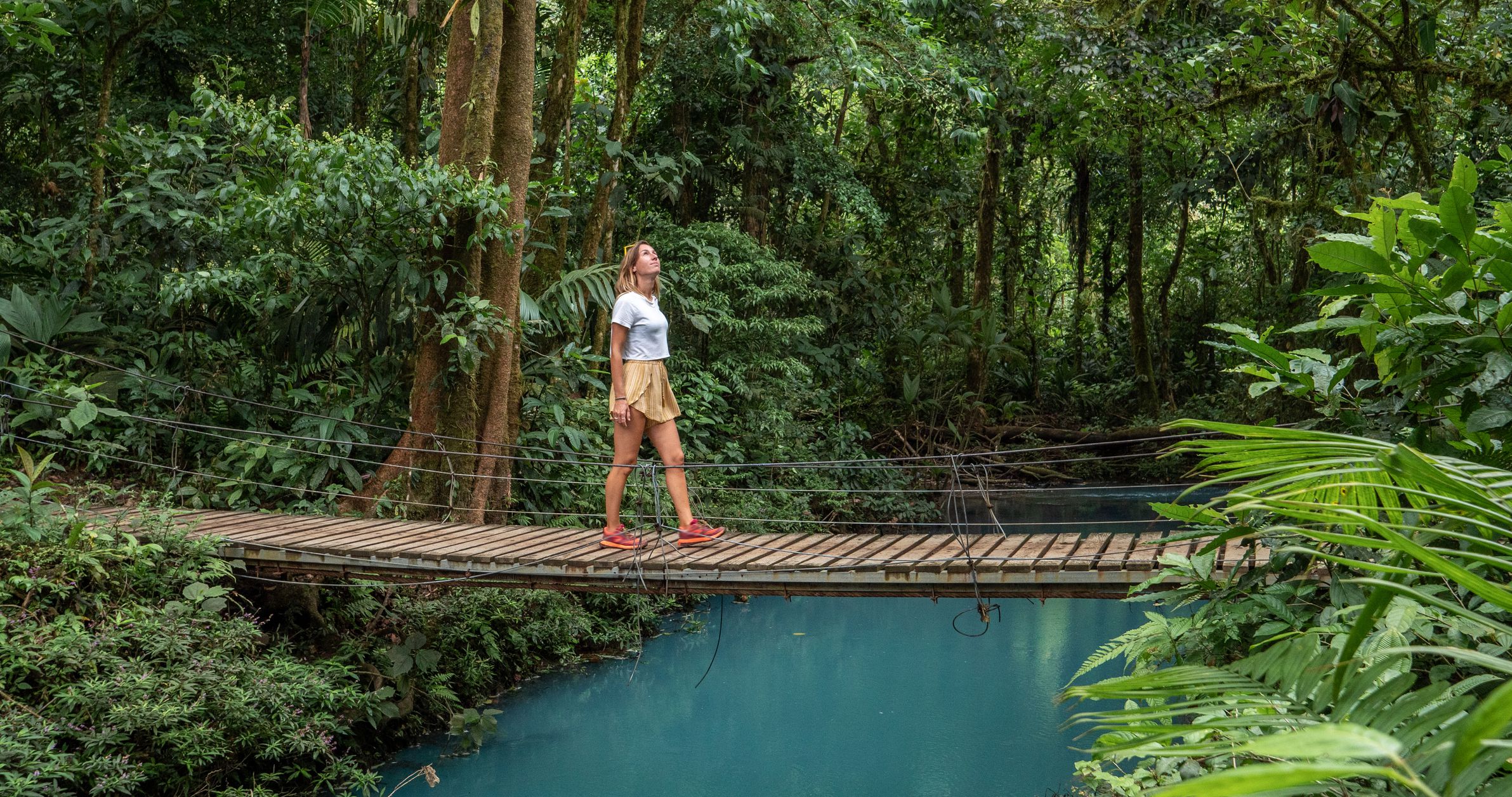 Young woman wandering in tropical rainforest walking on bridge over turquoise lagoon, Costa Rica